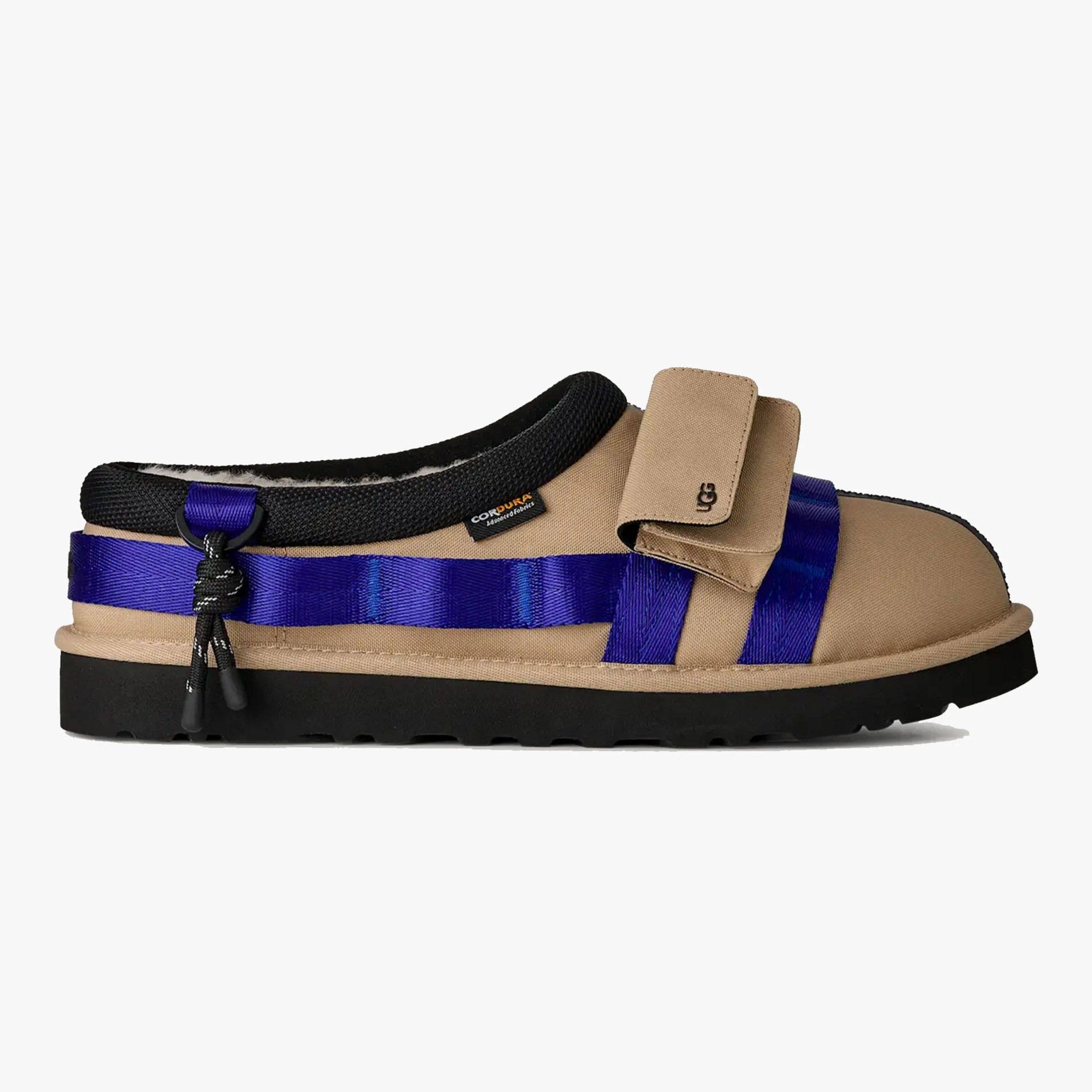 Tan slip-on shoe with black sole, black padded collar, blue straps, and UGG logo on the front strap.