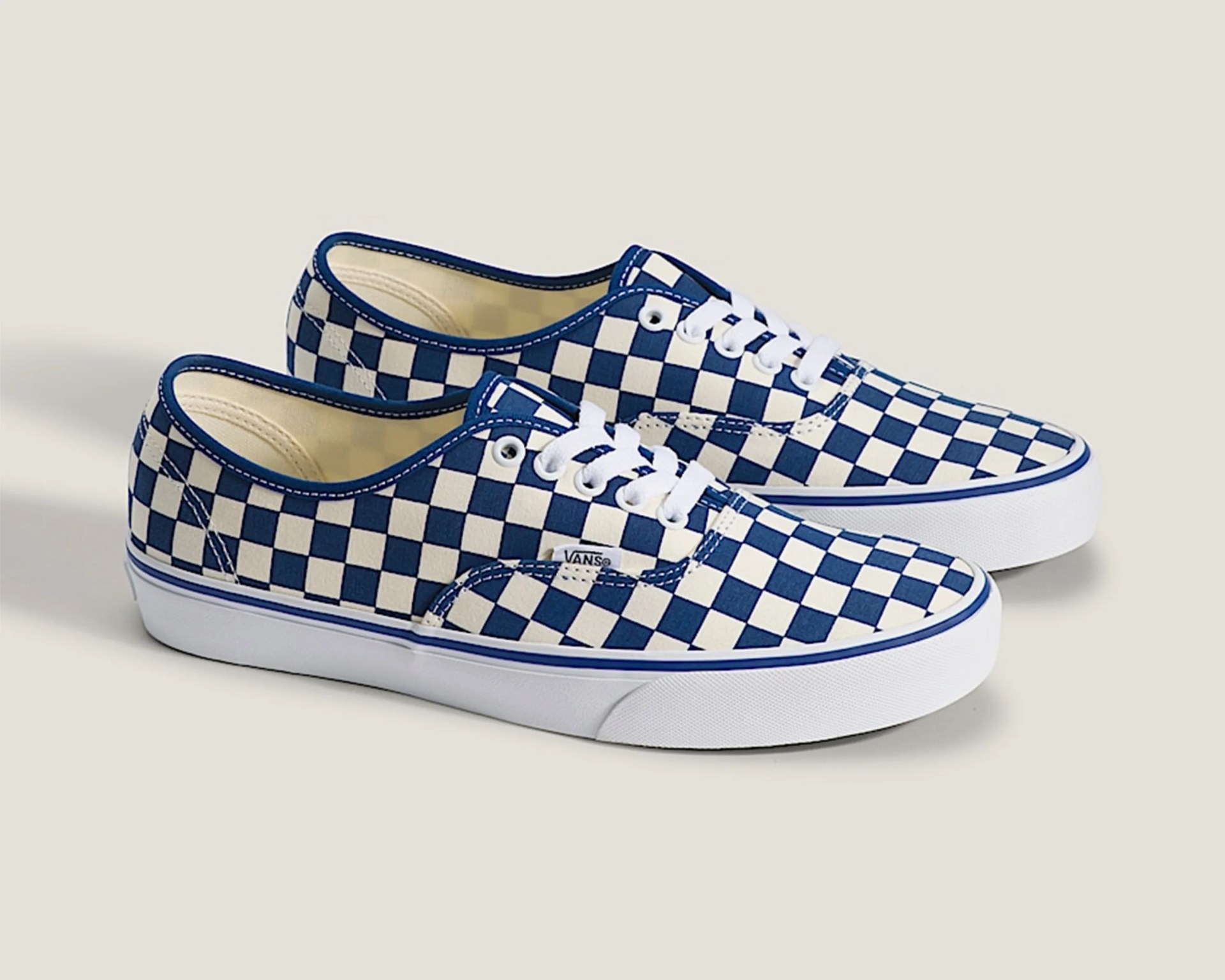 Pair of blue and white checkered Vans sneakers with white laces and white rubber soles on a beige background.