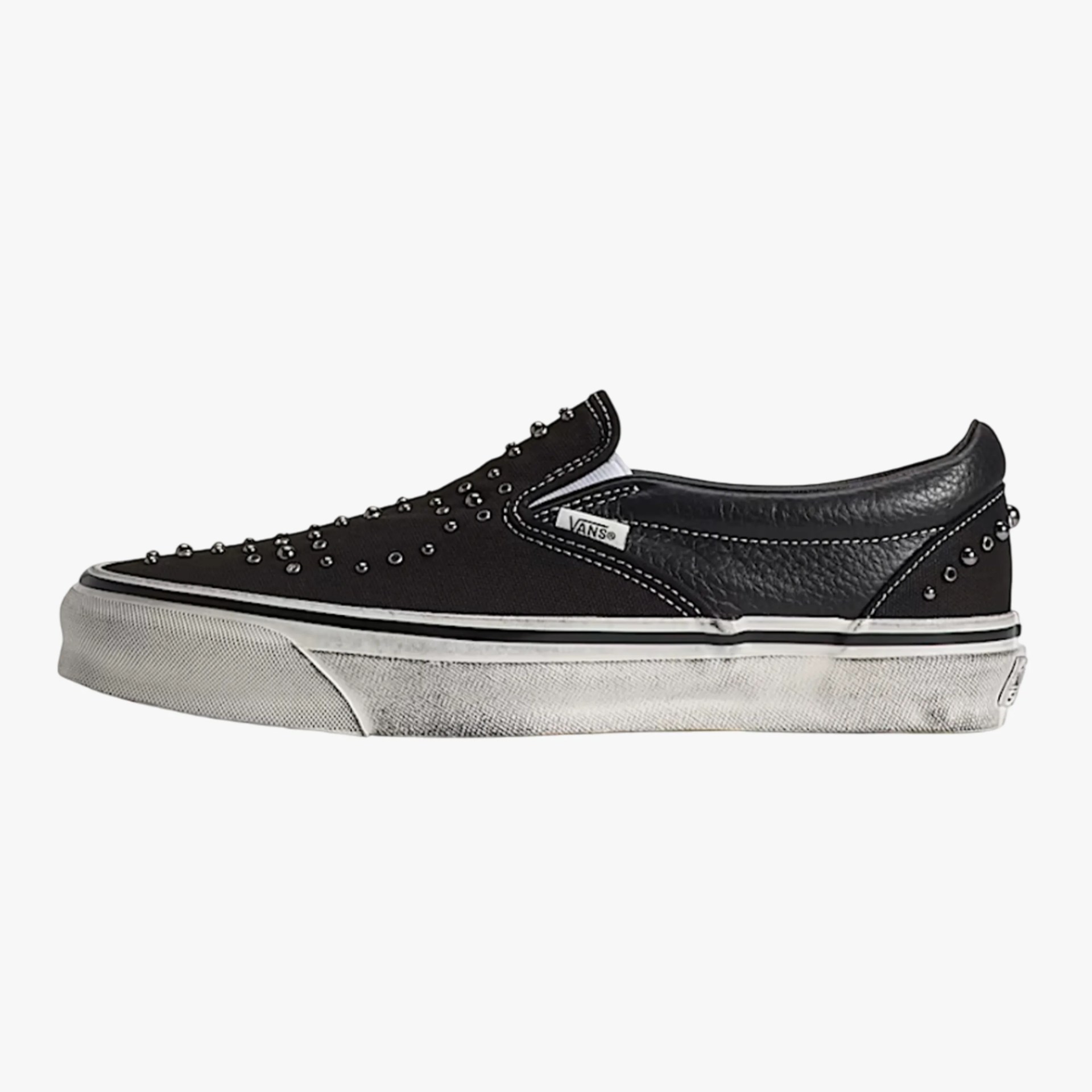 Black Vans slip-on sneaker with silver studs, white midsole with black stripe, and textured leather heel panel.