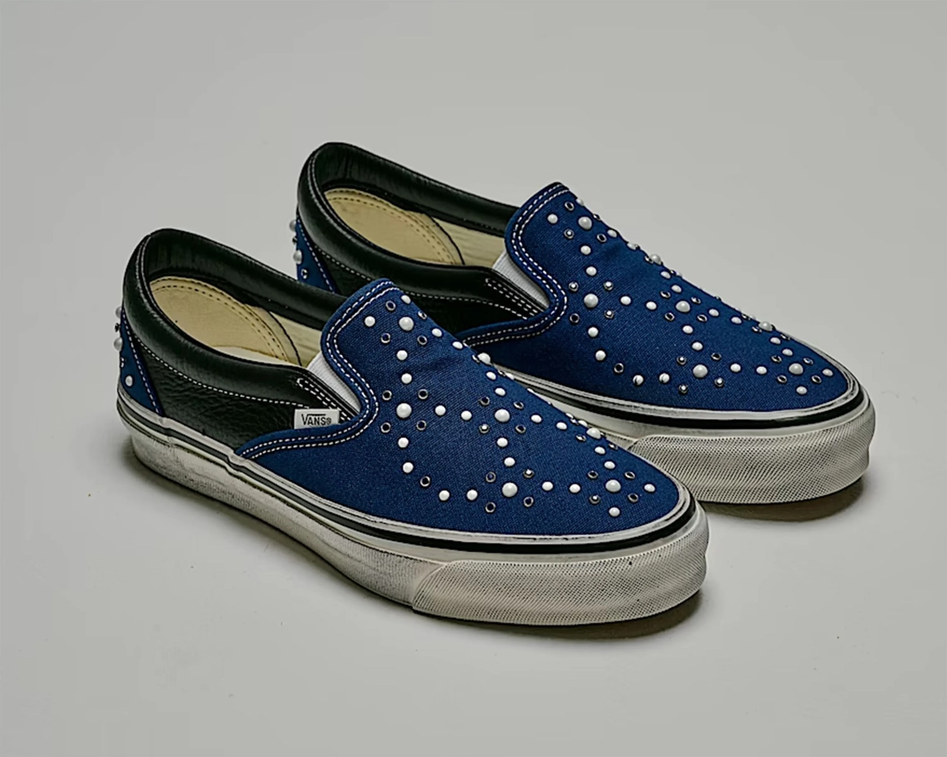 Pair of blue Vans slip-on shoes with black leather heel, white rubber soles, and pearl-like studs on top.