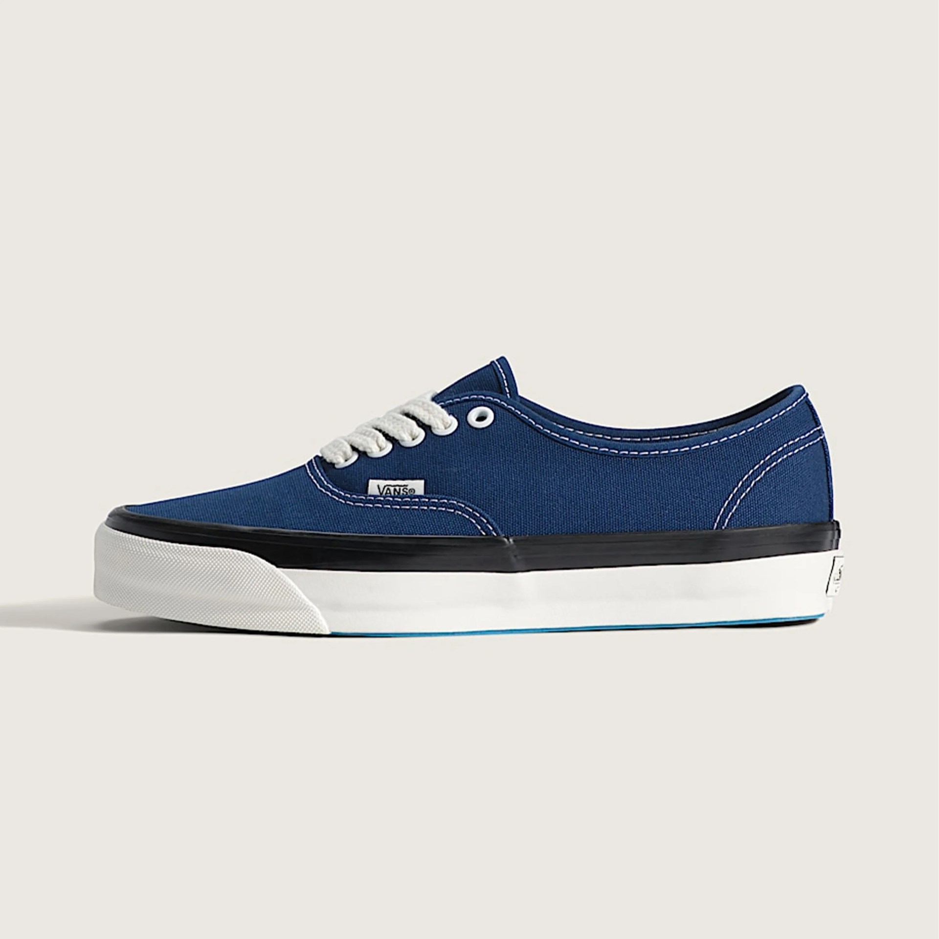 Blue canvas Vans sneaker with white laces, black trim, and white rubber sole.