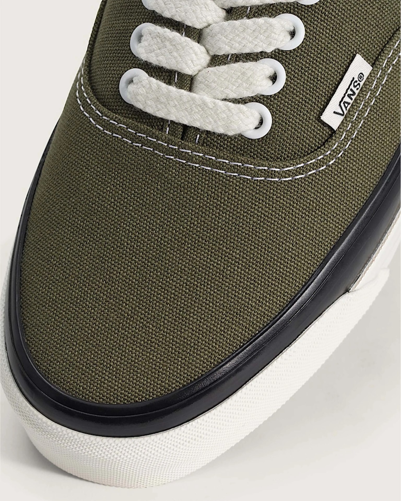 Close-up of olive green Vans sneaker with white laces, white stitching, black trim, and white rubber sole.