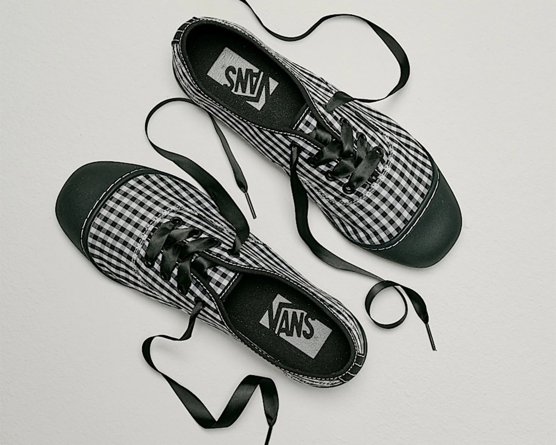 Pair of black and white checkered Vans sneakers with black satin laces on a white surface.
