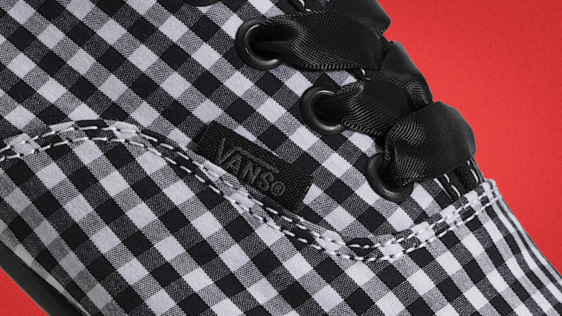 Close-up of a black and white checkered Vans shoe with black satin laces and visible stitching.