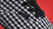Close-up of a black and white checkered Vans shoe with black satin laces and visible stitching.