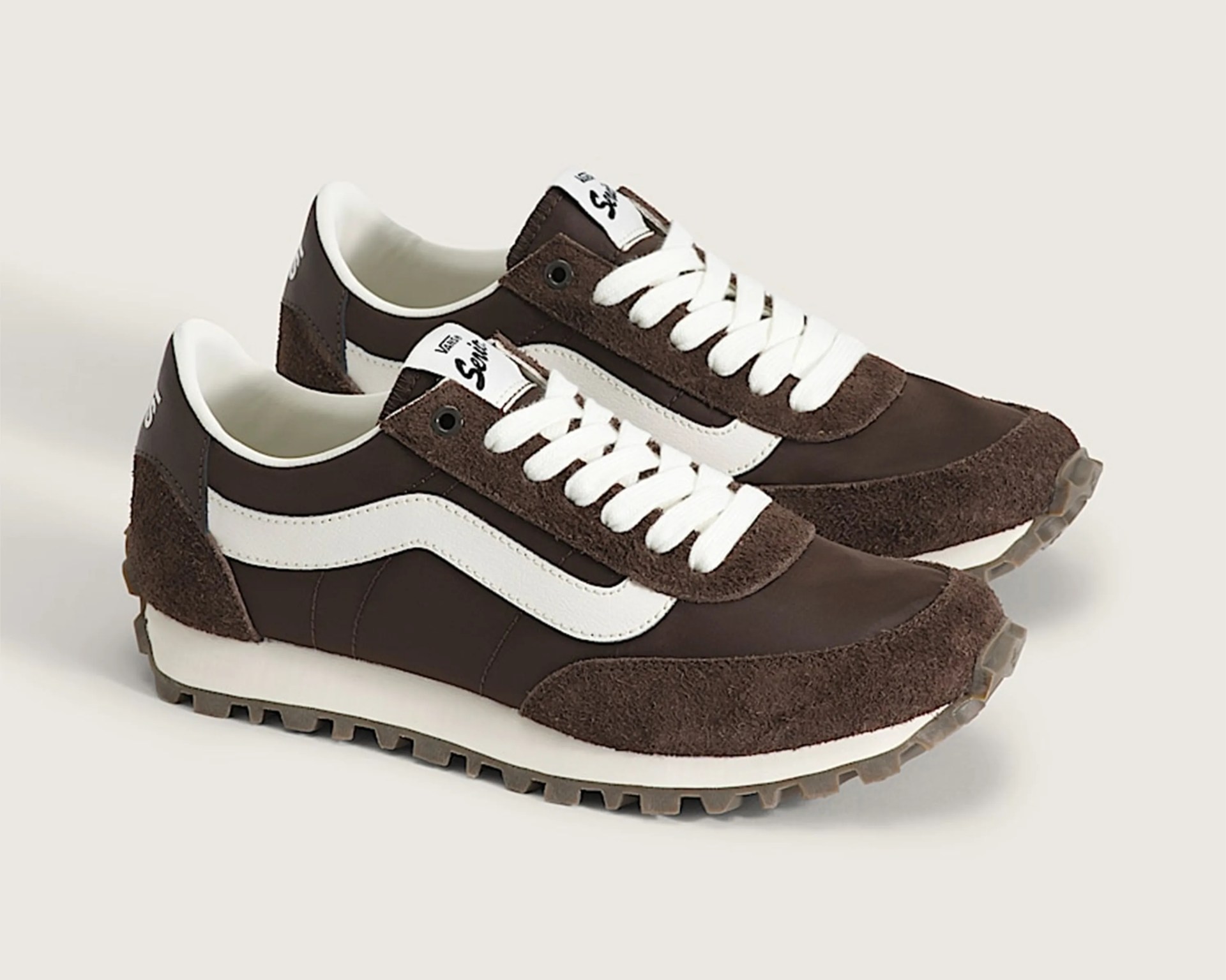 Pair of brown and white Vans sneakers with suede accents and white laces on a light background.
