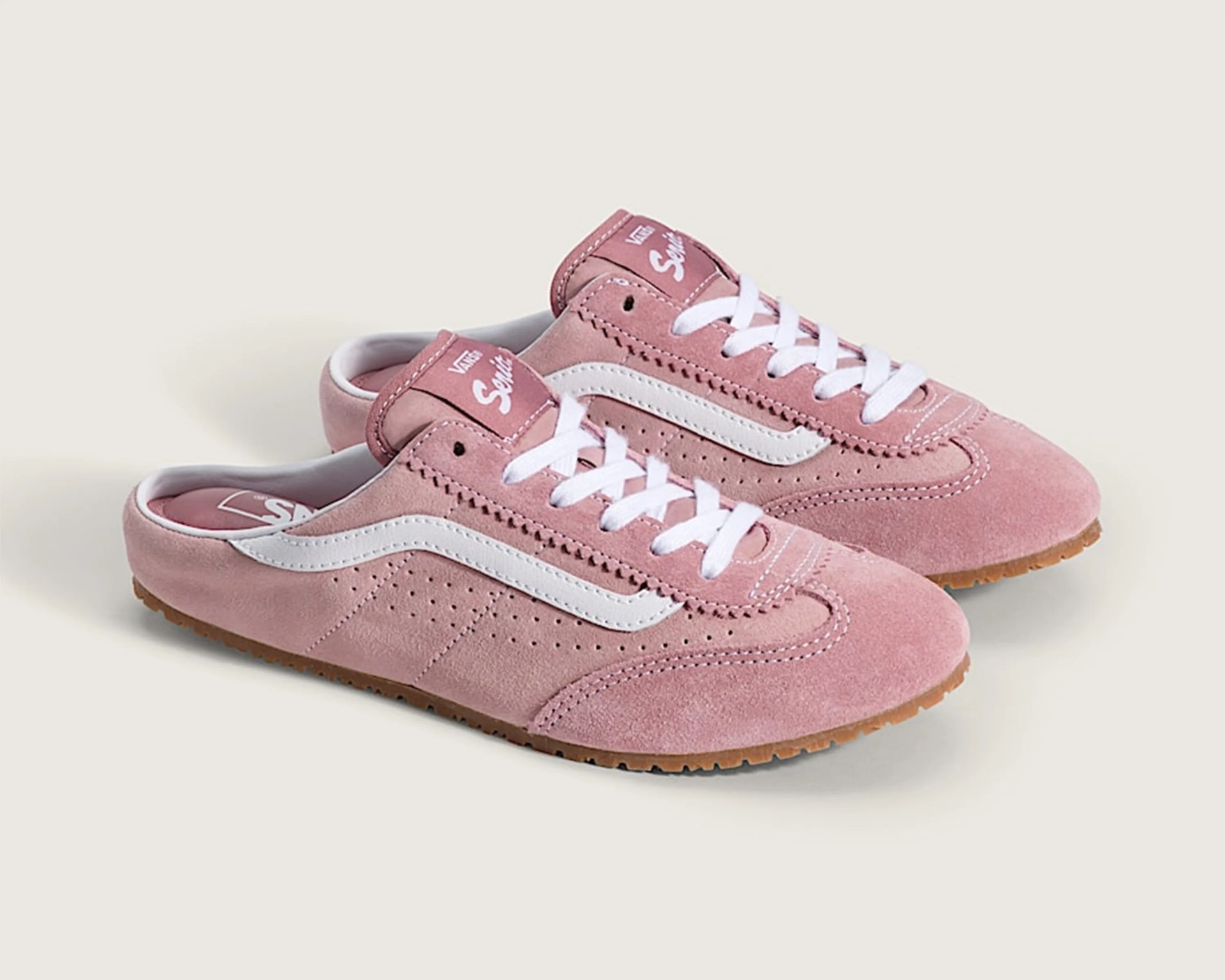 Pair of pink suede Vans sneakers with white side stripe and laces on a light background.