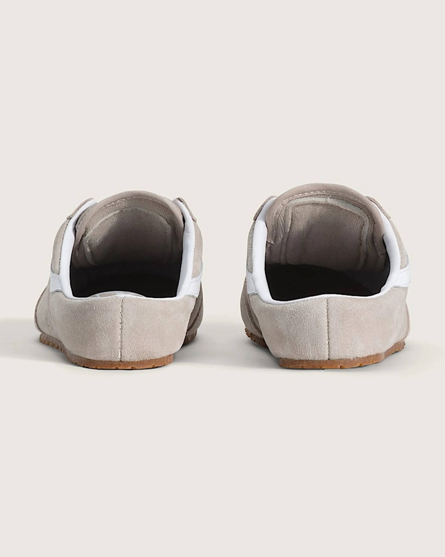 Pair of beige suede slip-on shoes with white trim and brown soles, viewed from the back.