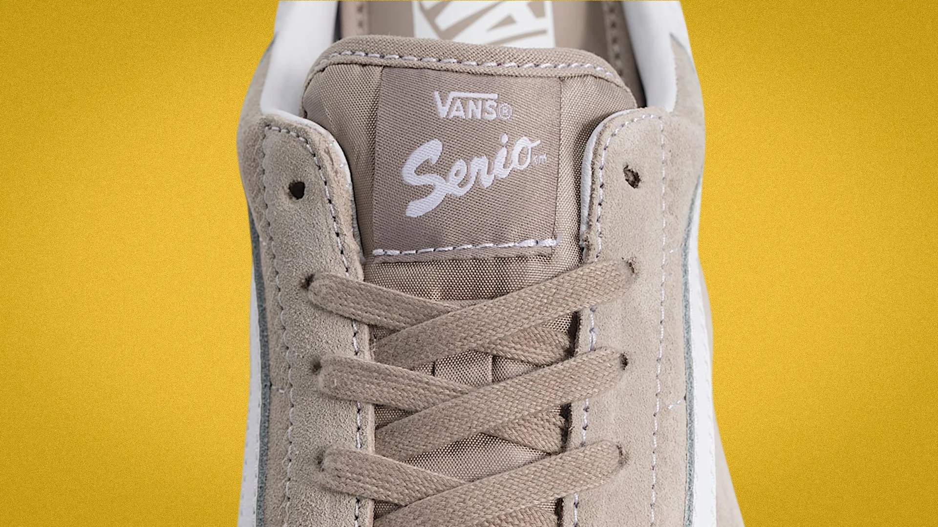 Close-up of beige Vans Serio sneaker tongue with beige laces against a yellow background.