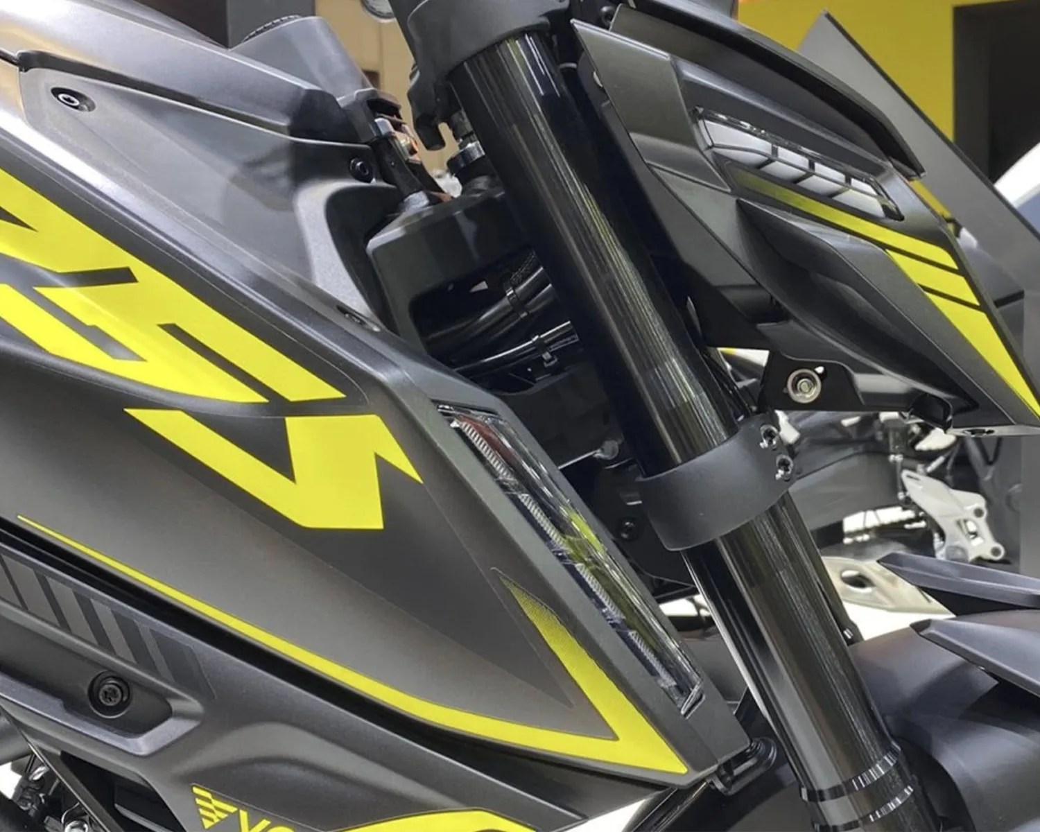 Close-up of a black and yellow motorcycle front fork and side panel with angular design and integrated light.