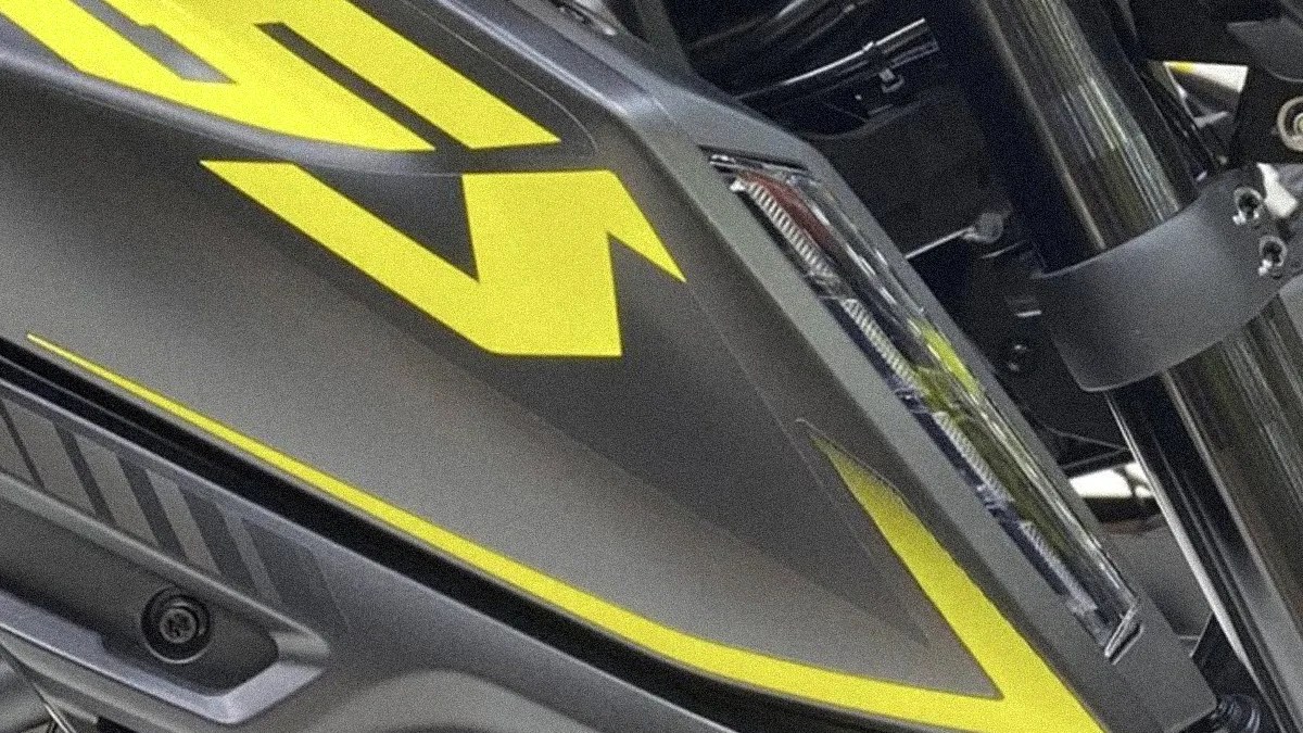 Close-up of a matte gray motorcycle fuel tank with bright yellow angular graphics and a black frame component.