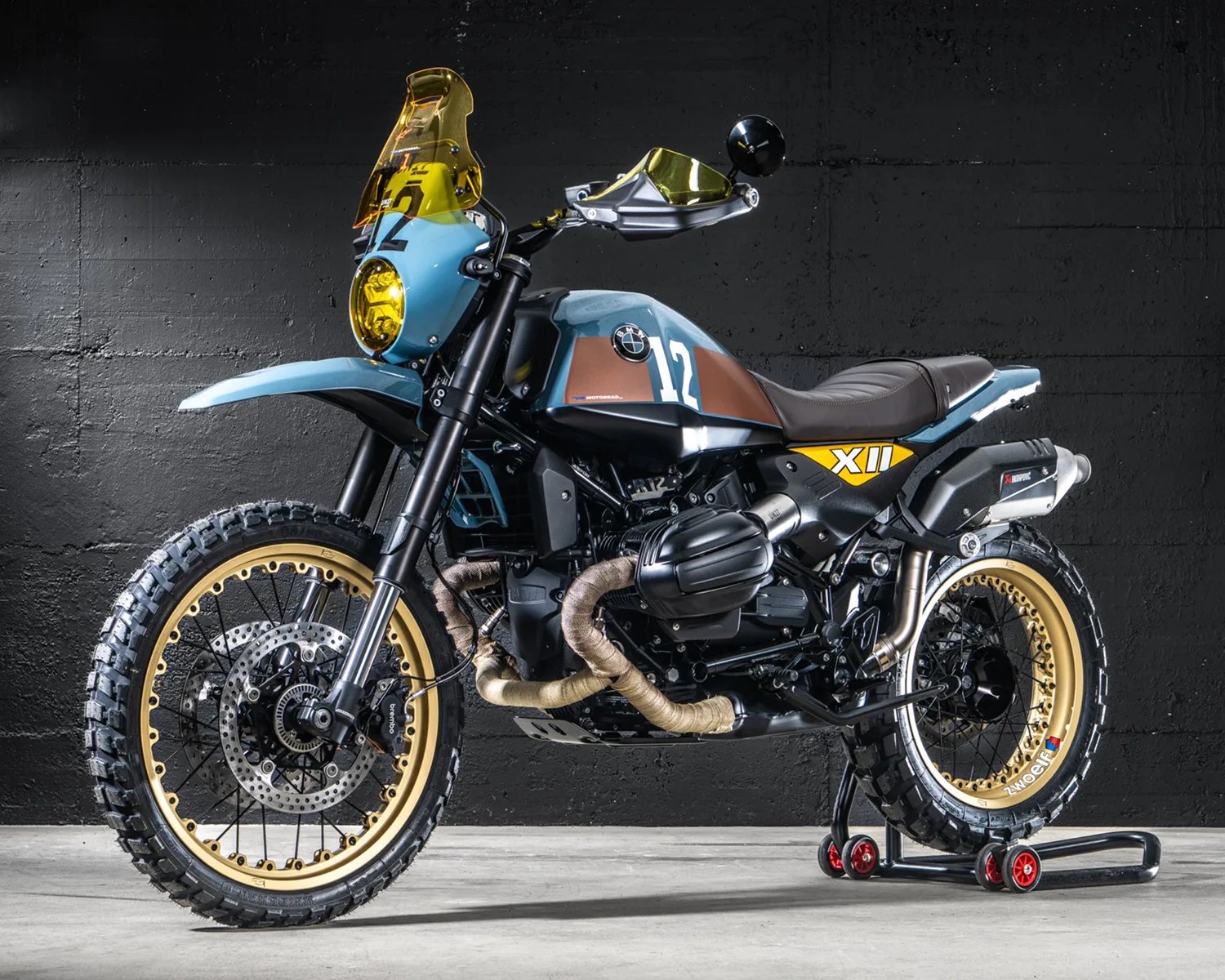 Blue and brown BMW motorcycle with yellow tinted windshield and headlight, knobby tires, and gold rims on a stand.