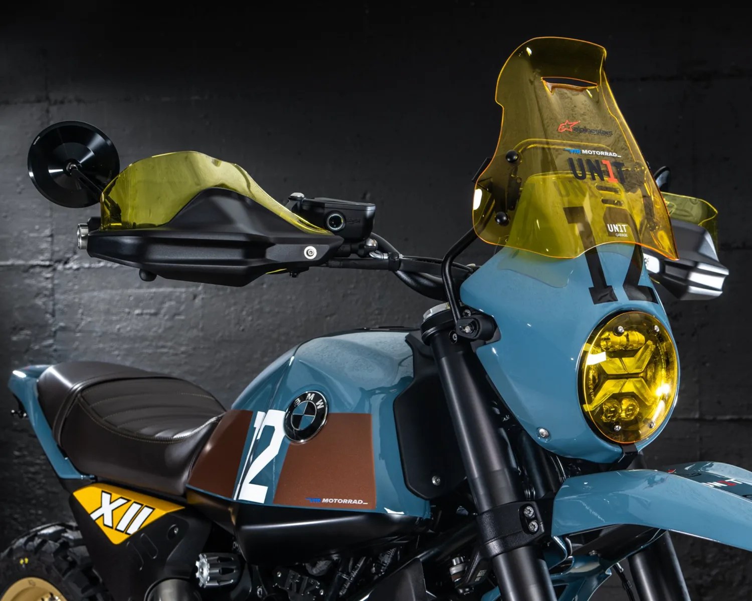 Blue BMW motorcycle with yellow tinted windshield, headlight, and handguards, featuring number 12 and XII decals.