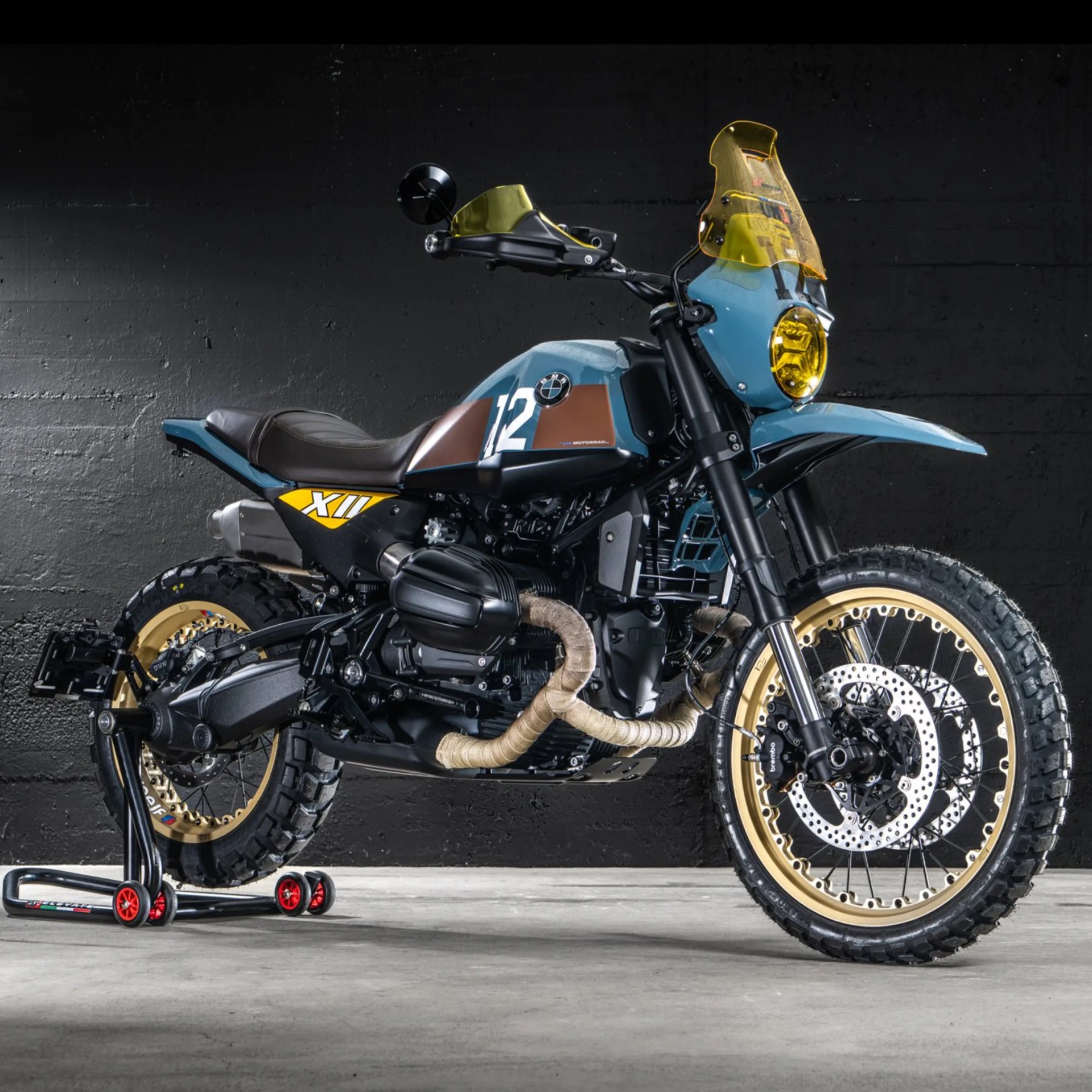 Blue and brown BMW R nineT motorcycle with yellow windshield and headlight, gold rims, and knobby tires on a stand.