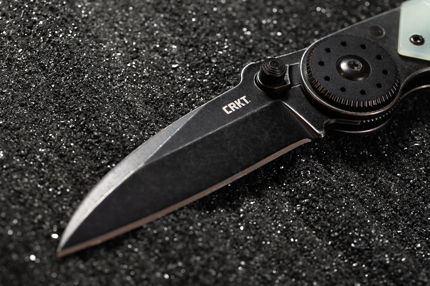 Black folding knife blade with "CRKT" logo on a textured black surface.
