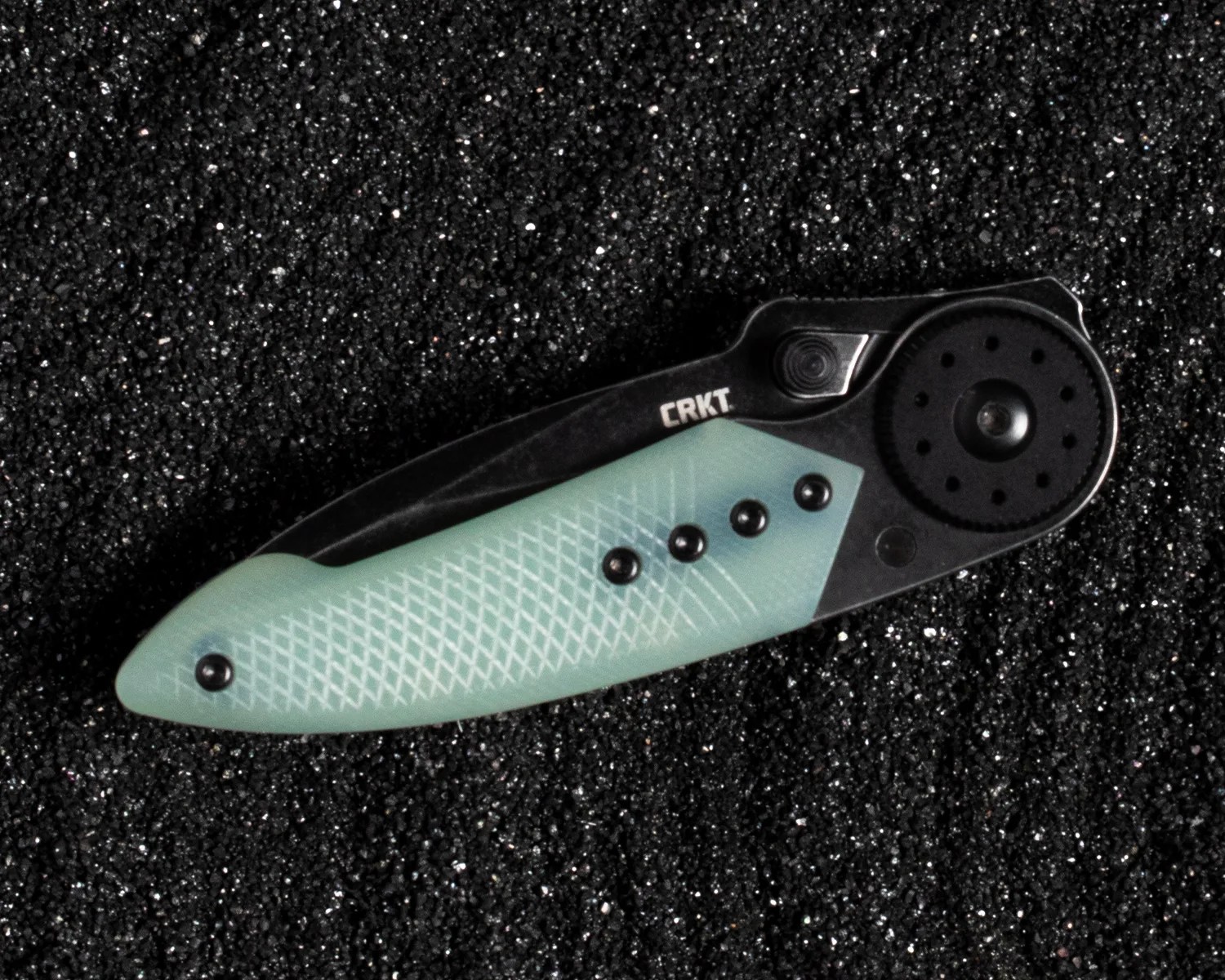 Folded black and light blue CRKT pocket knife with textured handle on black granular surface.