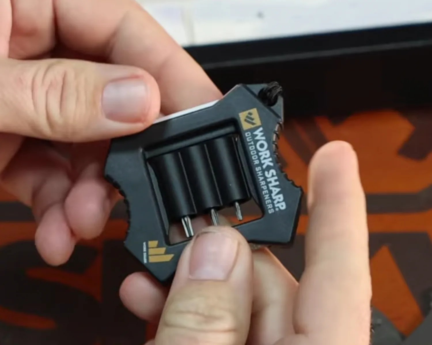 Black compact Work Sharp outdoor sharpener with three cylindrical sharpening rods held in two hands.