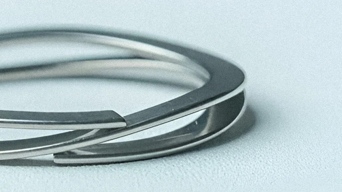 Close-up of two overlapping silver metal bangles on a light textured surface.