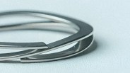 Close-up of two overlapping silver metal bangles on a light textured surface.