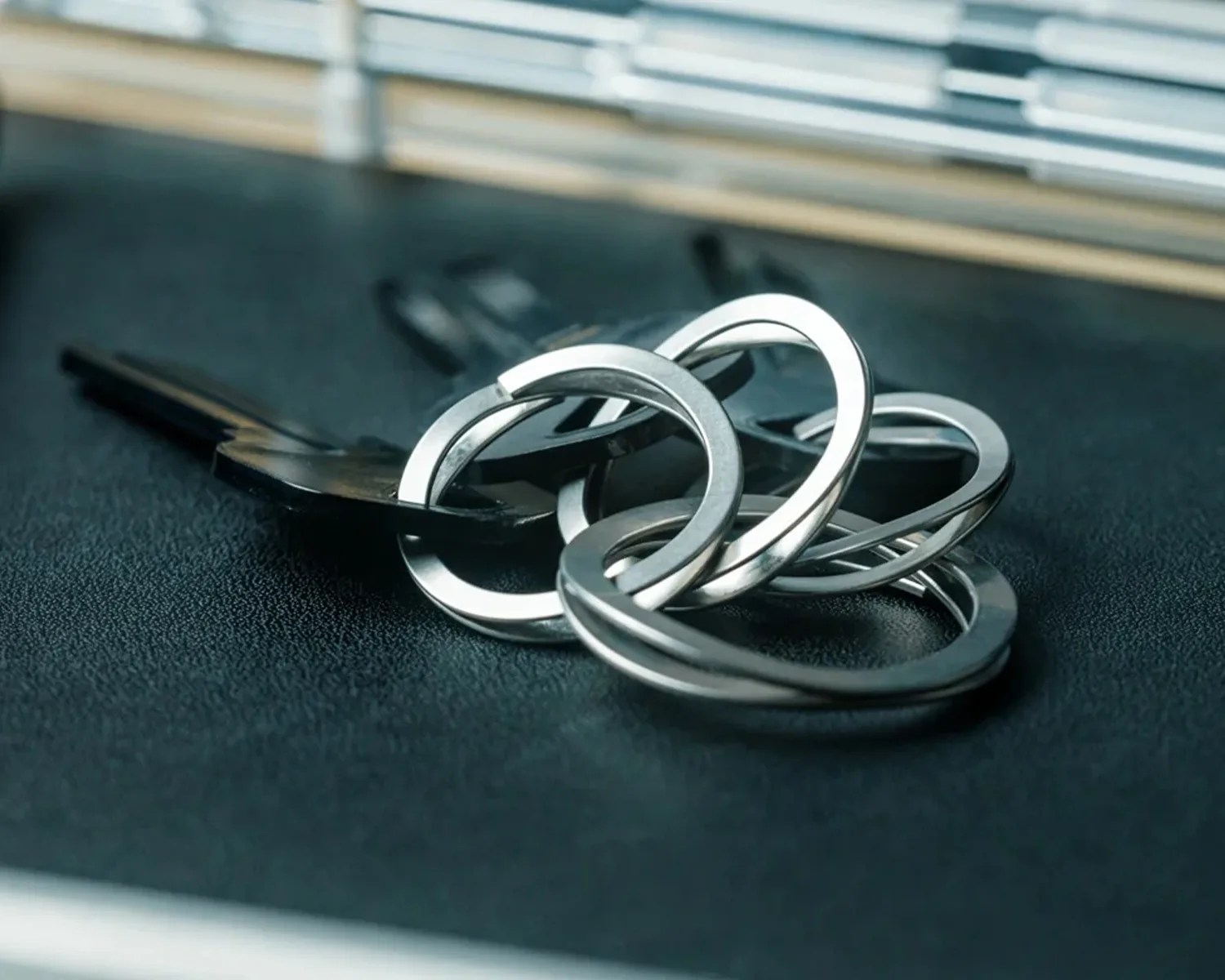 Set of silver metal keys with multiple linked key rings on a dark textured surface.