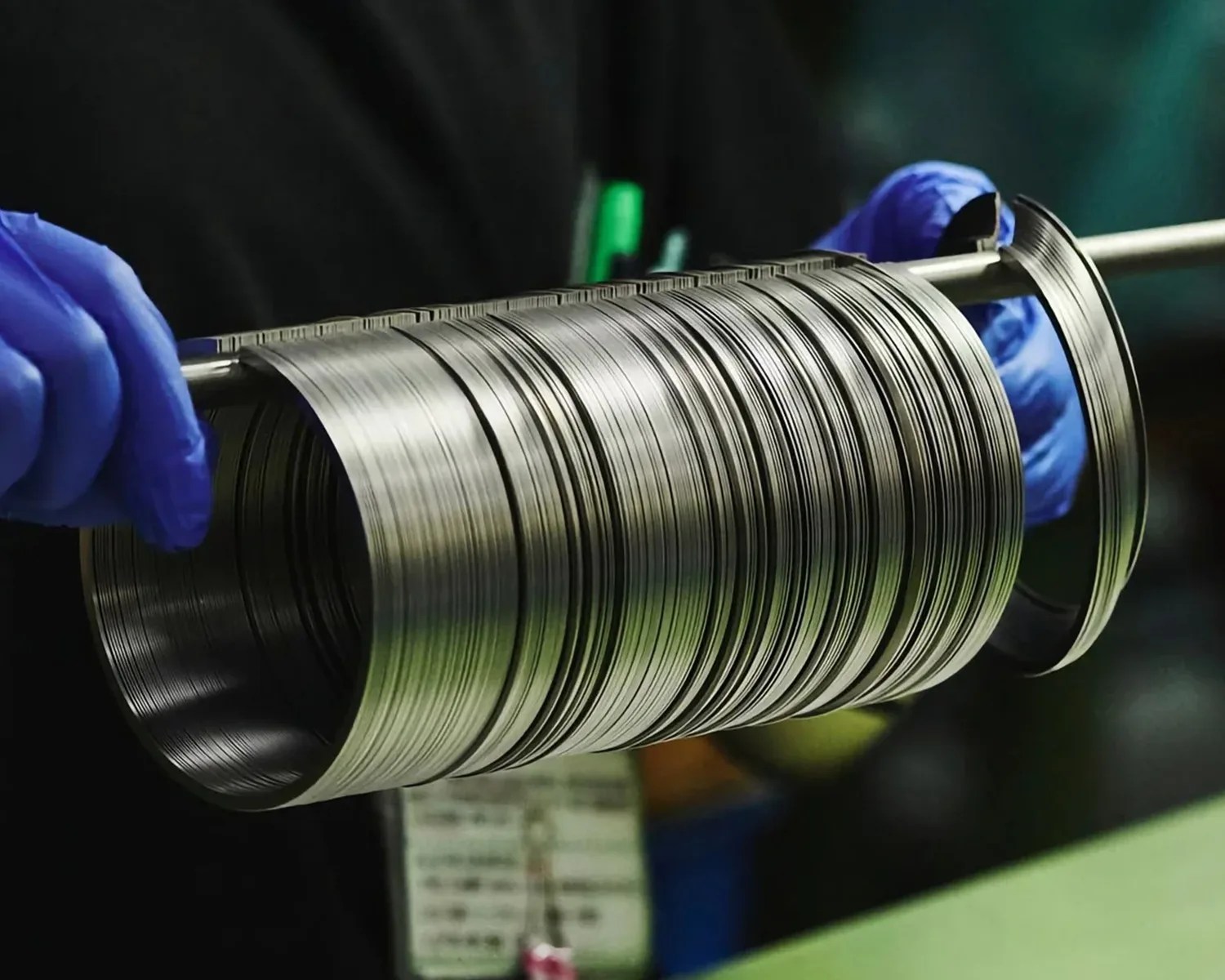 Stack of thin, shiny metal rings held on a rod by hands wearing blue gloves.