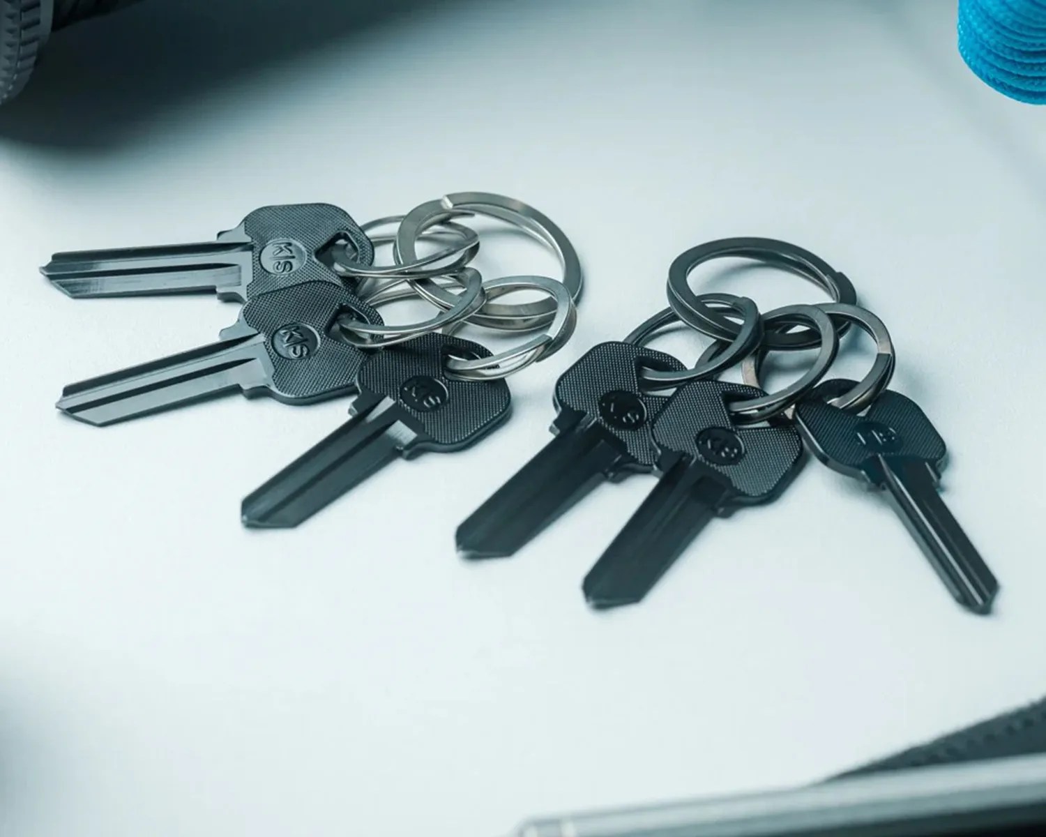 Two sets of black keys on silver key rings placed on a white surface.