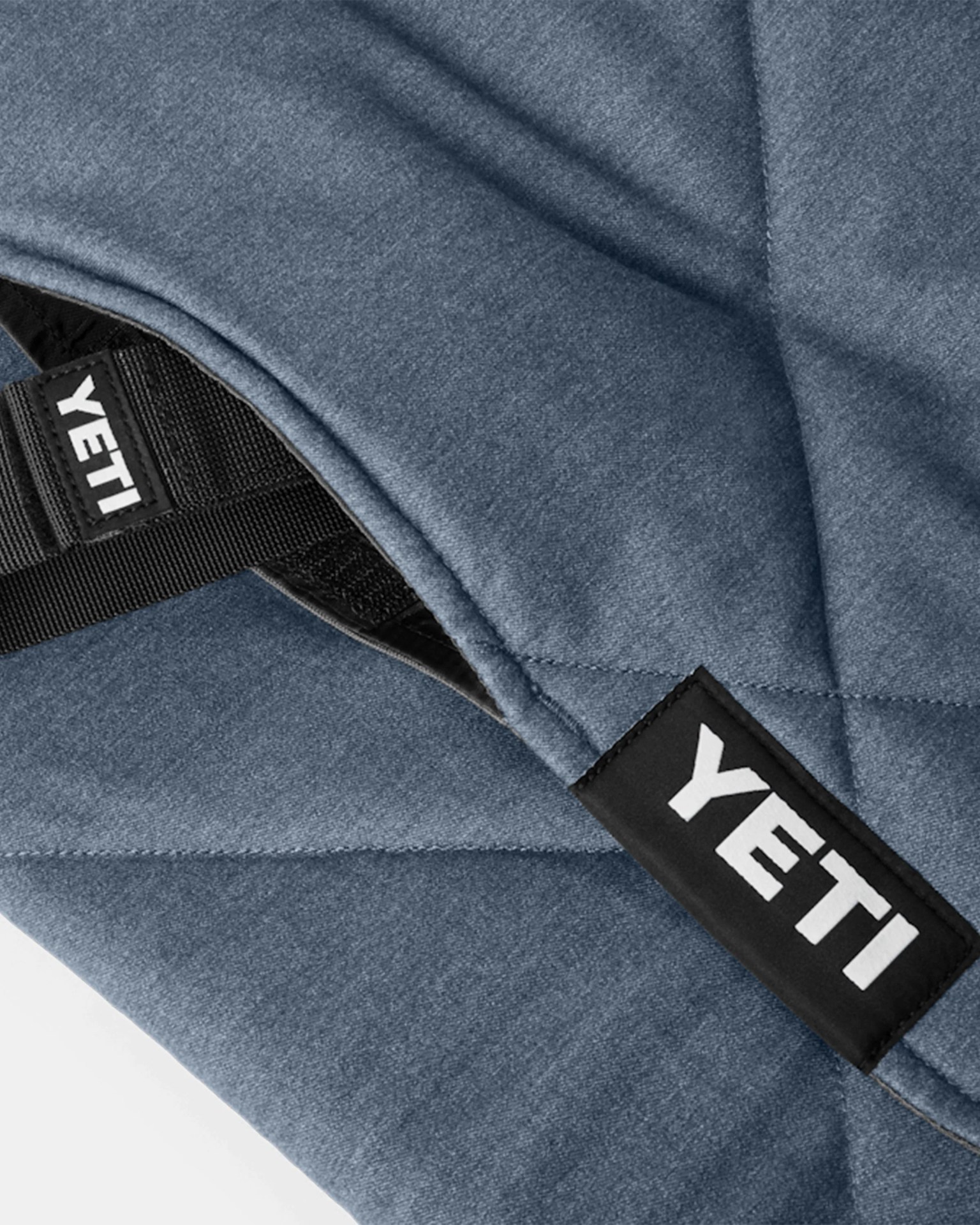Close-up of blue quilted fabric with black straps featuring white YETI logos.