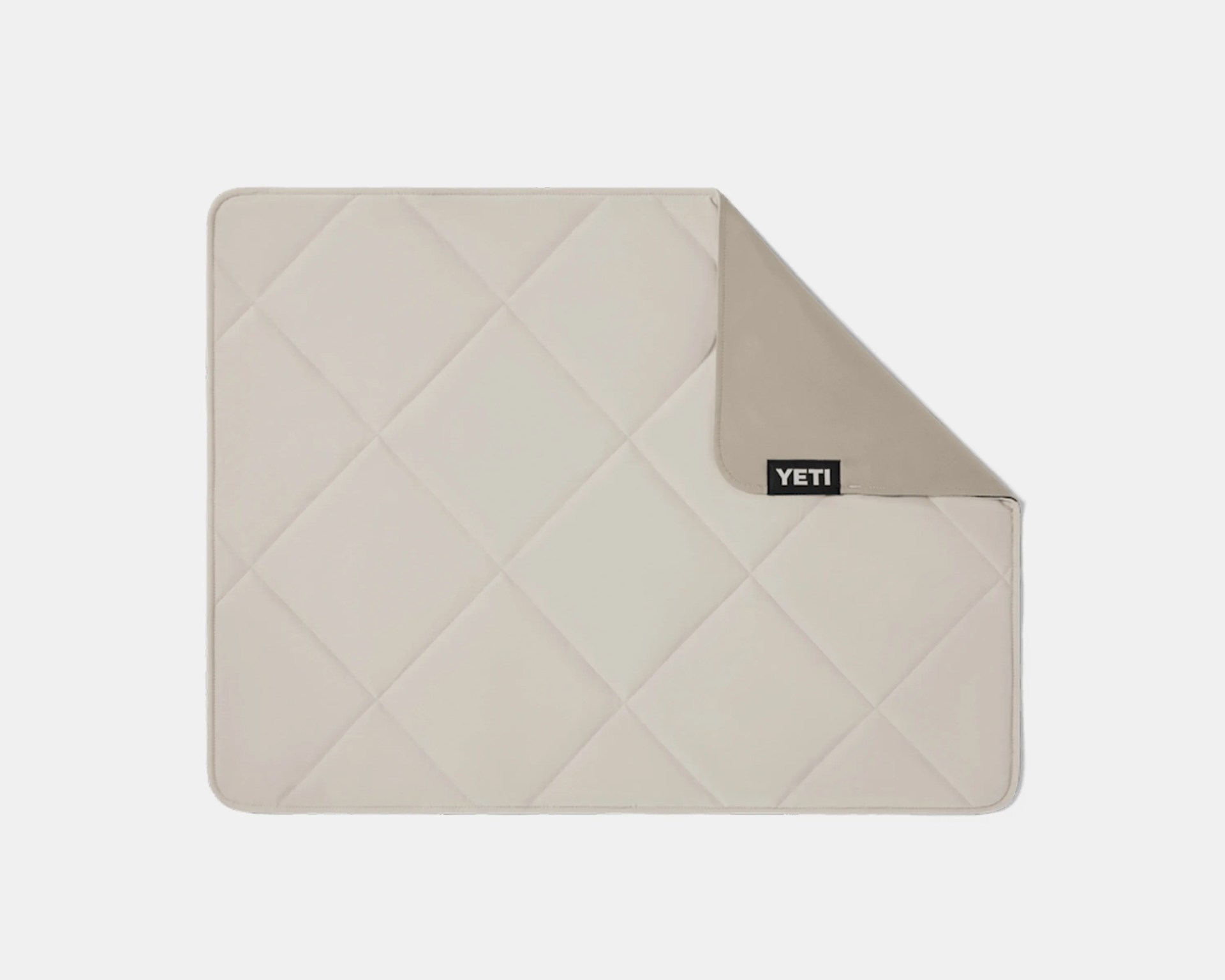 Beige quilted rectangular mat with a folded corner showing a solid beige underside and a black YETI logo tag.