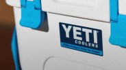 White YETI cooler with blue latches and logo reading "Wildly stronger! Keep ice longer!
