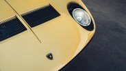 Close-up of a yellow Lamborghini hood with black vents and a round headlight on a dark asphalt surface.