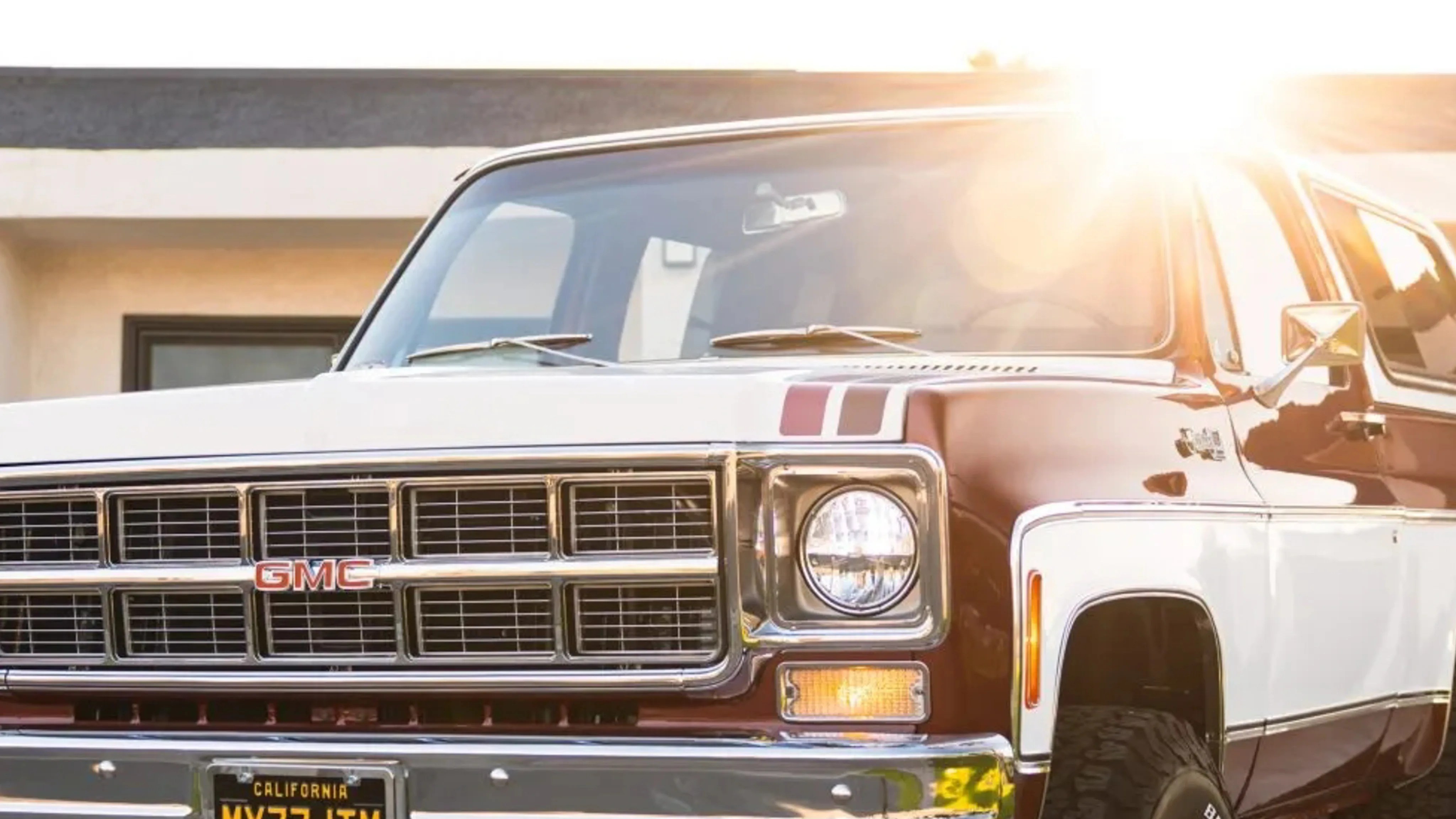 Front view of a two-tone brown and white vintage GMC truck with California license plate in sunlight.