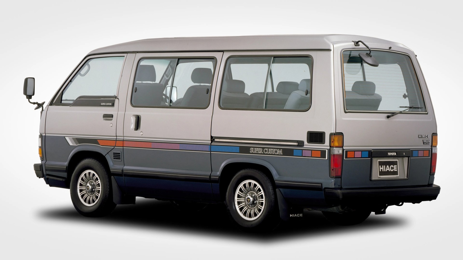 Two-tone gray Toyota Hiace van with "Super Custom" decals and alloy wheels, viewed from the side and rear.