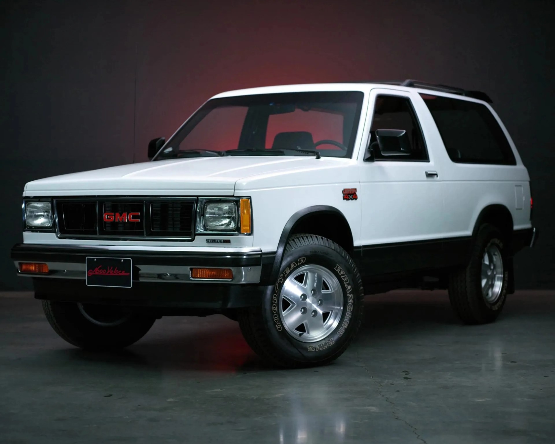 White GMC Jimmy 4x4 SUV with black trim and Goodyear Wrangler tires in a studio setting.
