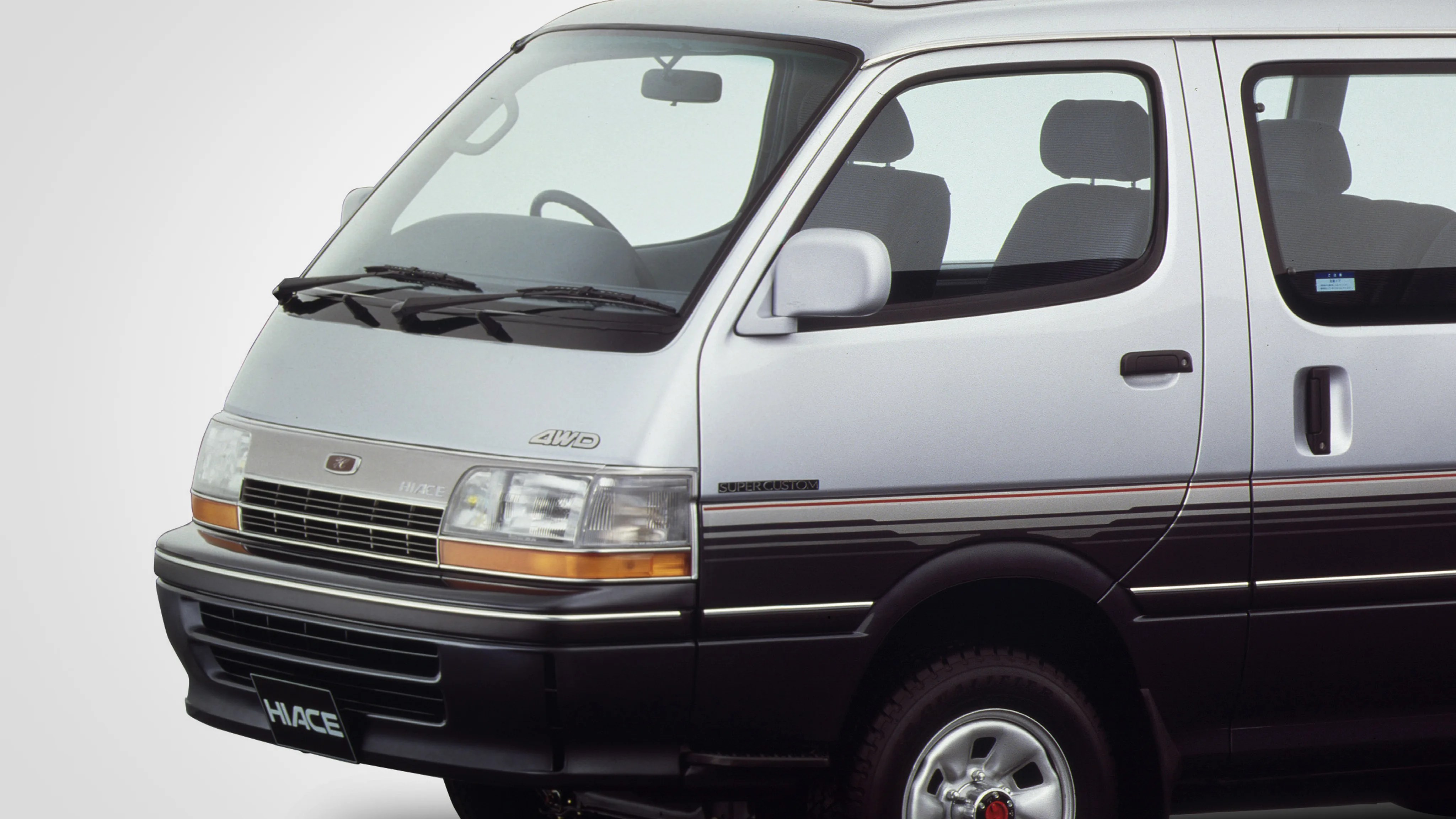 Silver and black Toyota Hiace van with 4WD badge and "Super Custom" trim, shown from front side.