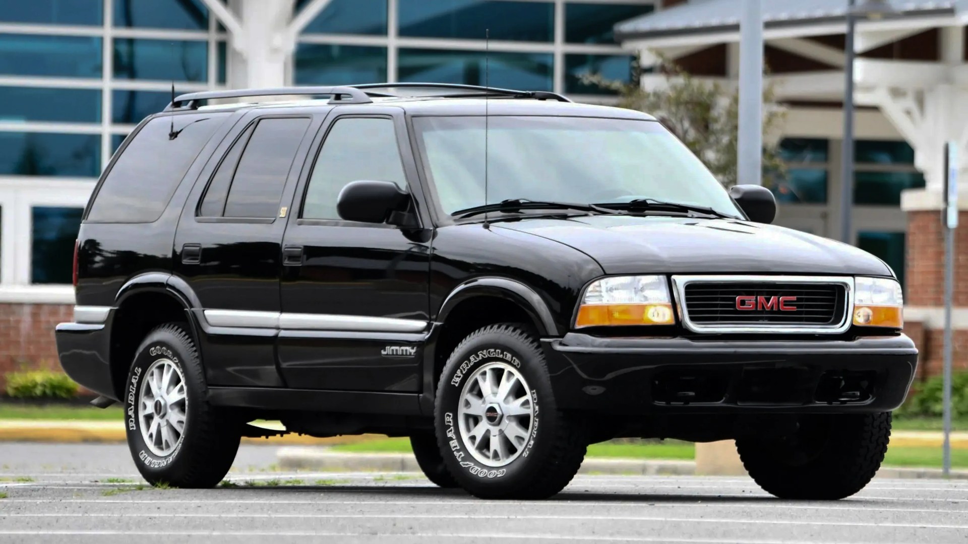 Black GMC Jimmy SUV with silver trim and Goodyear Wrangler tires parked in front of a building.