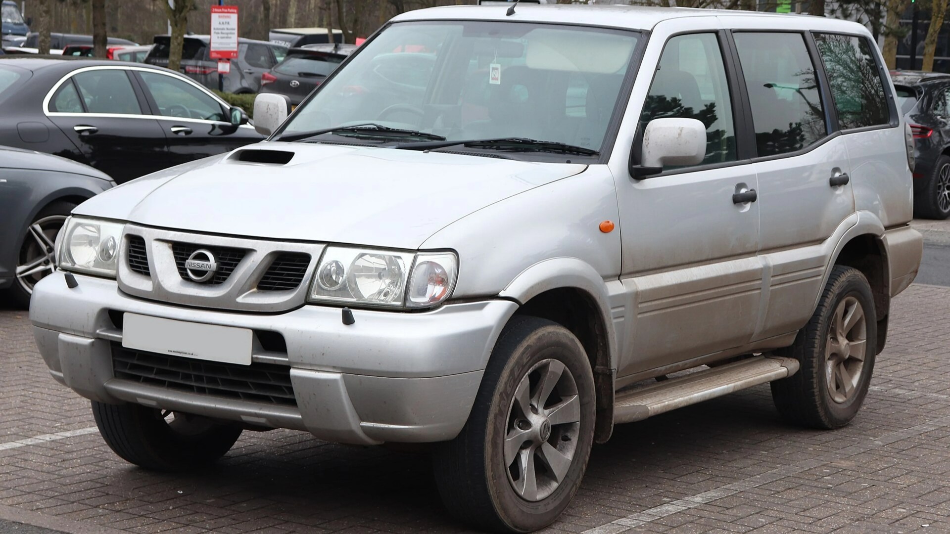 Silver Nissan SUV with visible dirt on the lower body parked in a lot.