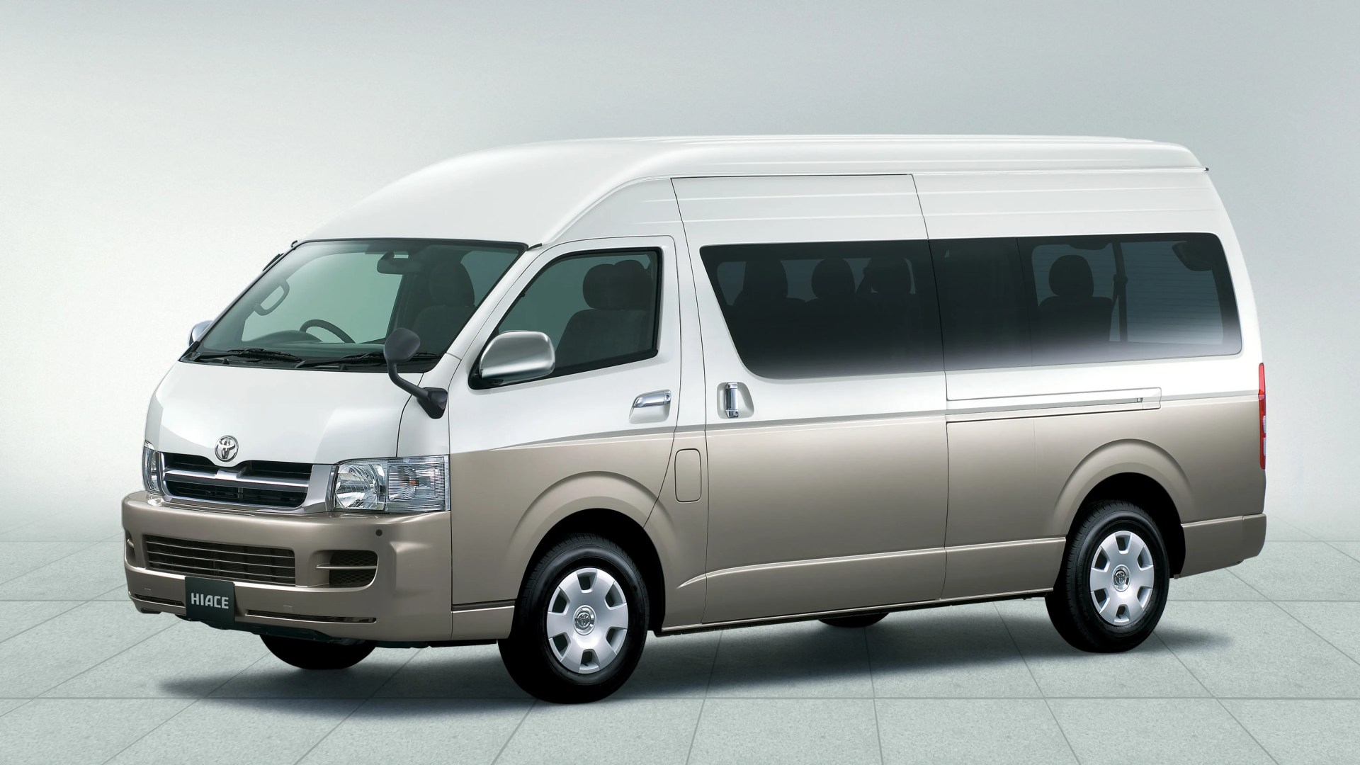 Two-tone beige and white Toyota Hiace van with tinted windows on a tiled floor.
