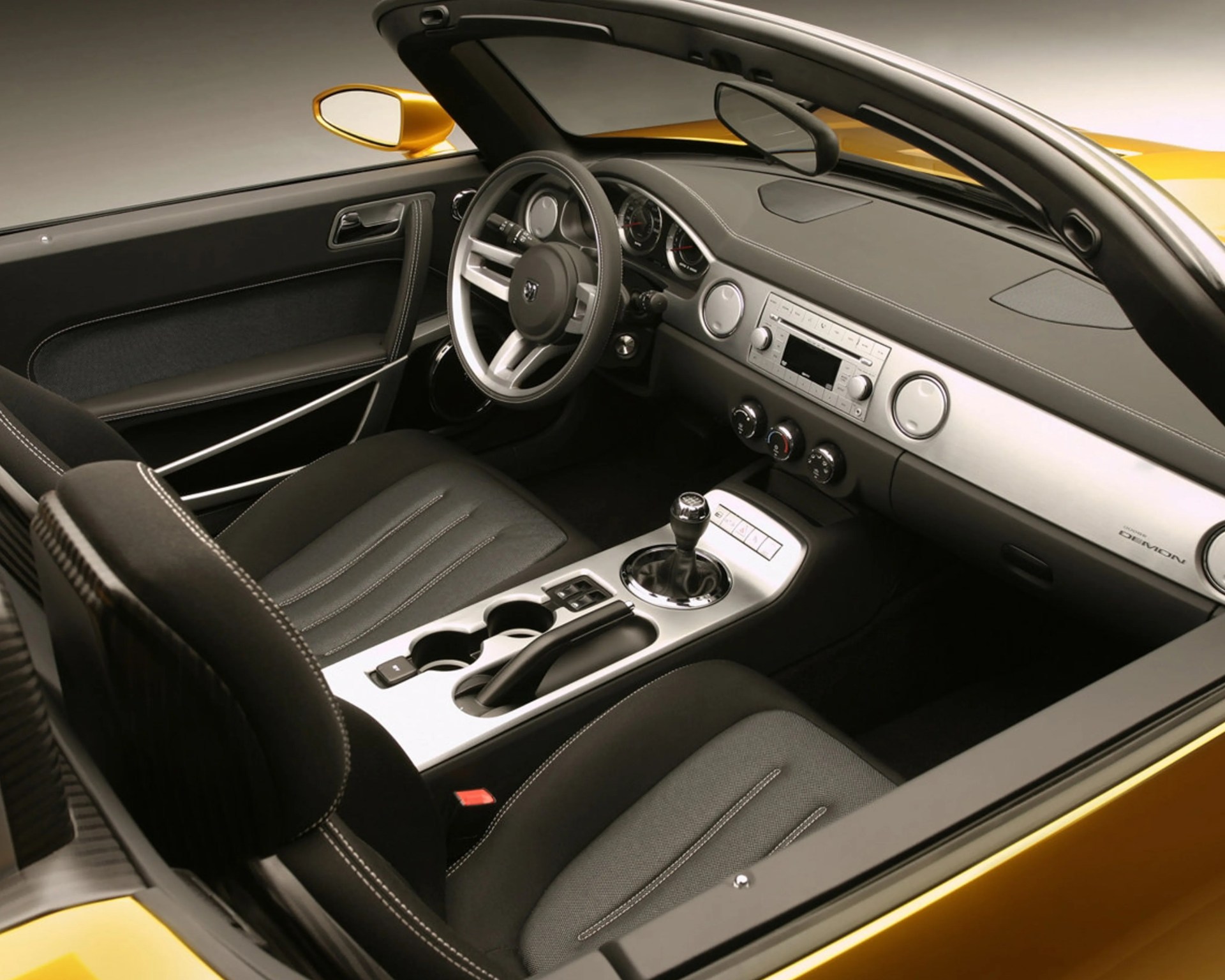 Interior of a yellow convertible sports car with black fabric seats, manual gear shift, and silver dashboard accents.