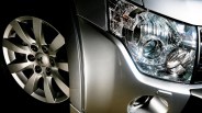 Close-up of a silver car's front wheel, fender, and clear headlight assembly.