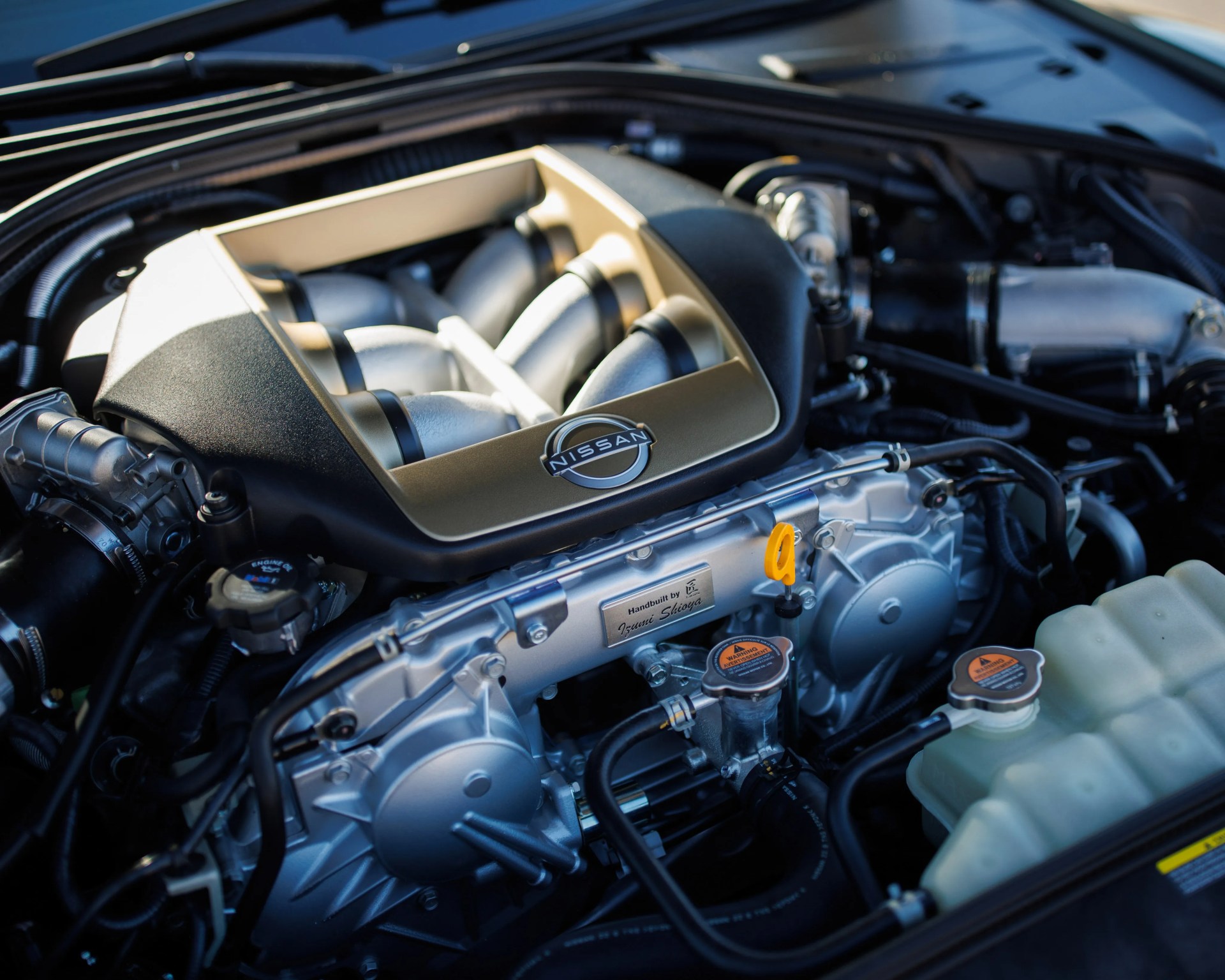 Close-up of a Nissan engine with a gold and black intake manifold and a plaque reading "Handbuilt by Izumi Shioya.