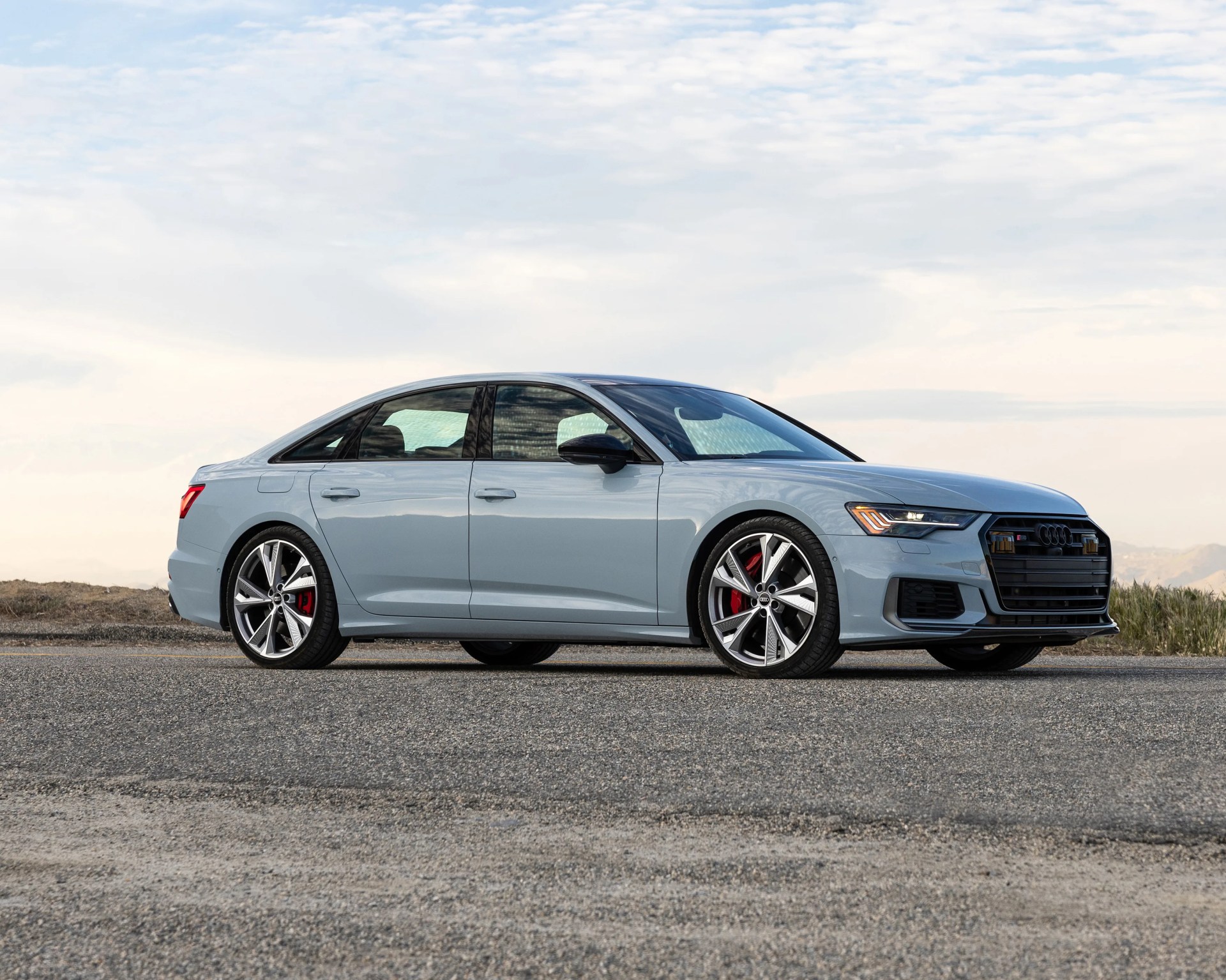 Light blue Audi S6 sedan with black roof and red brake calipers parked on asphalt under cloudy sky.
