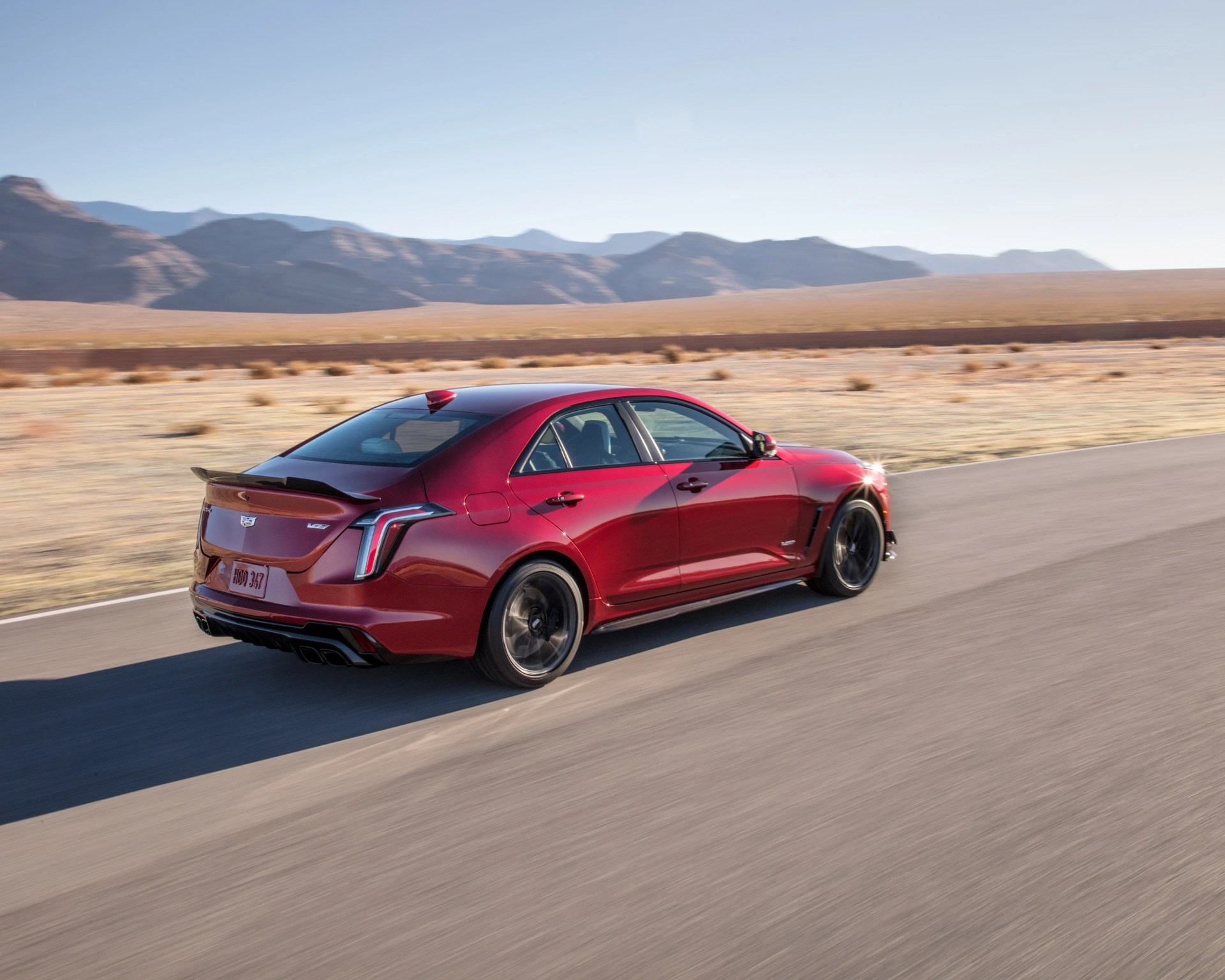 Red Cadillac V-Series sedan driving on a paved road with mountains in the background.