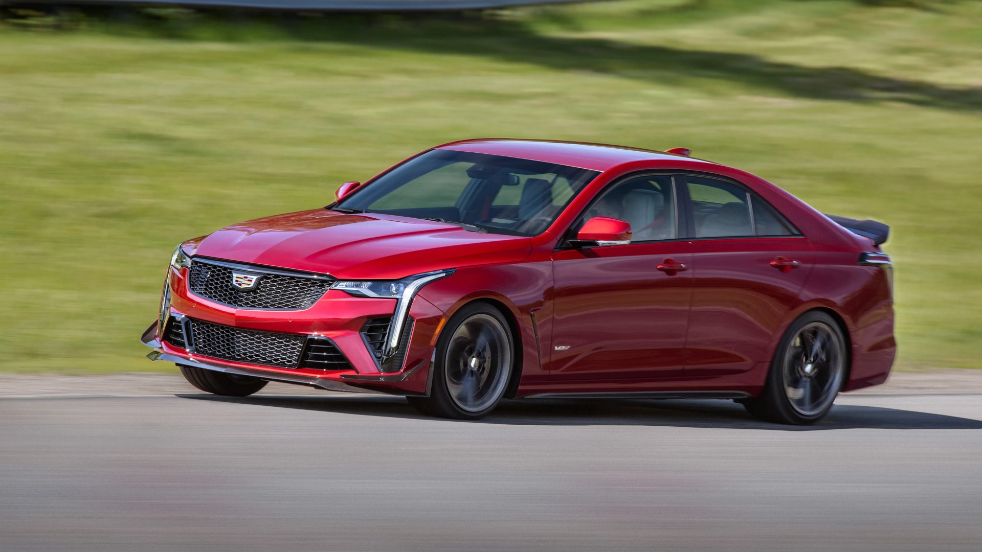 Red Cadillac CT5-V sedan with black wheels driving on a paved road with grass in the background.