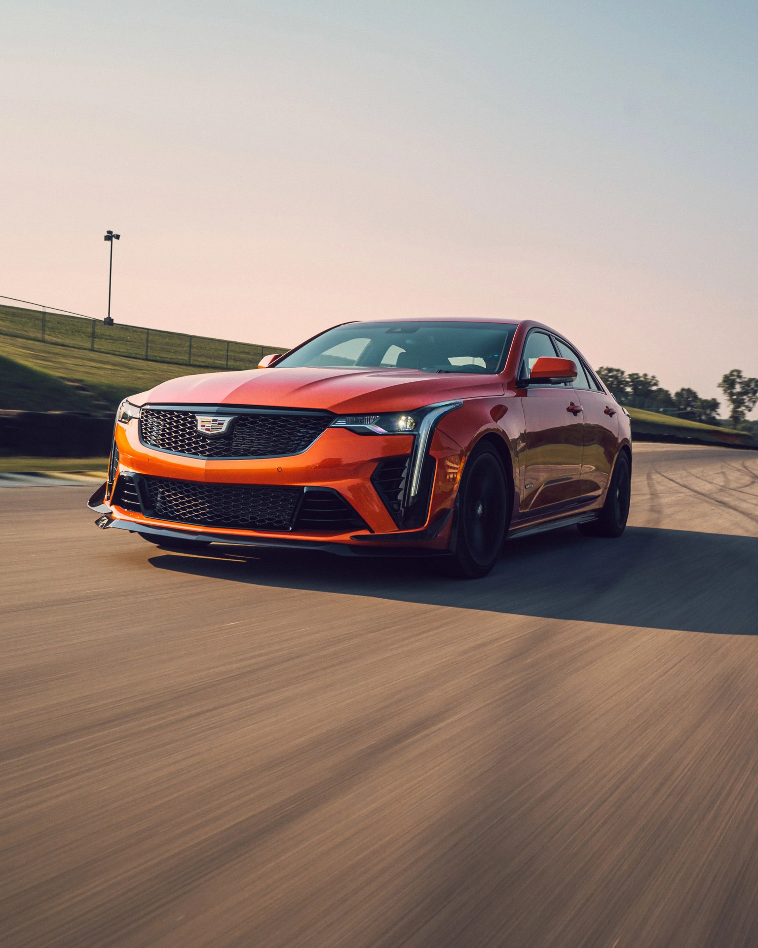 Orange Cadillac CT5-V sedan driving on a racetrack with black wheels and LED headlights.