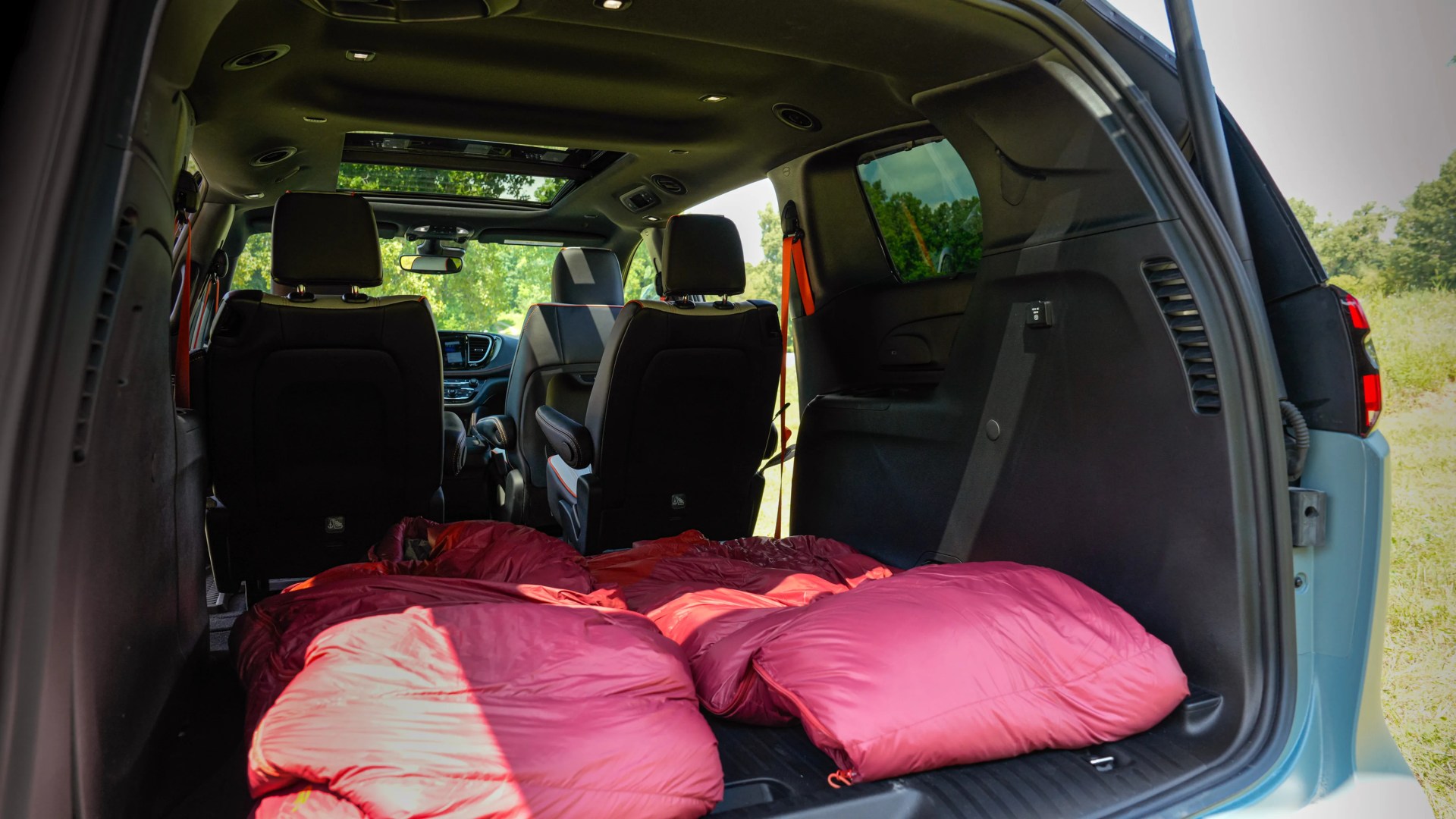 Red sleeping bags laid out in the rear cargo area of a vehicle with black interior and front seats visible.