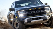 Black Ford pickup truck with headlights on driving off-road, kicking up dirt.