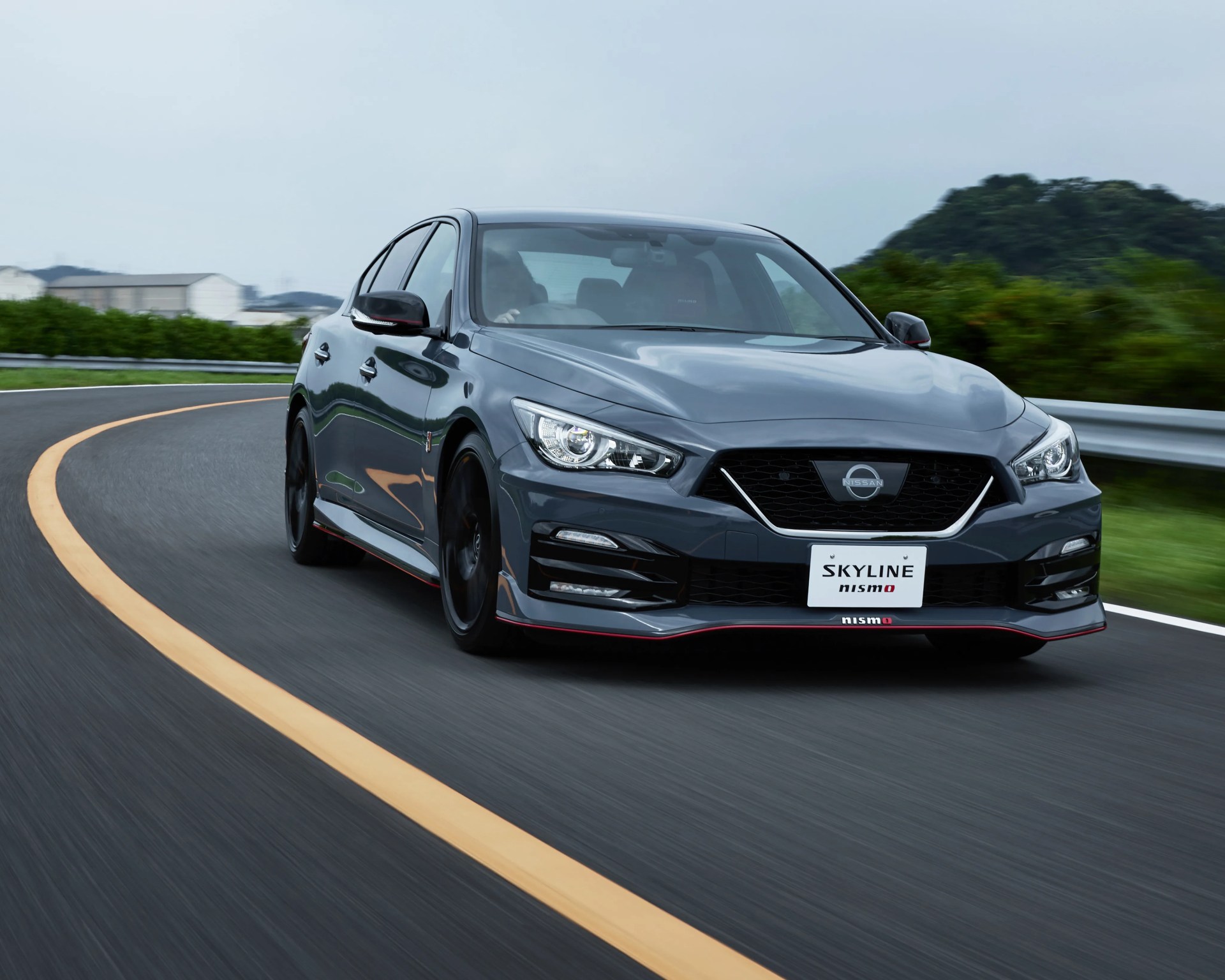 Dark gray Nissan Skyline Nismo sedan driving on a curved road with a yellow centerline.