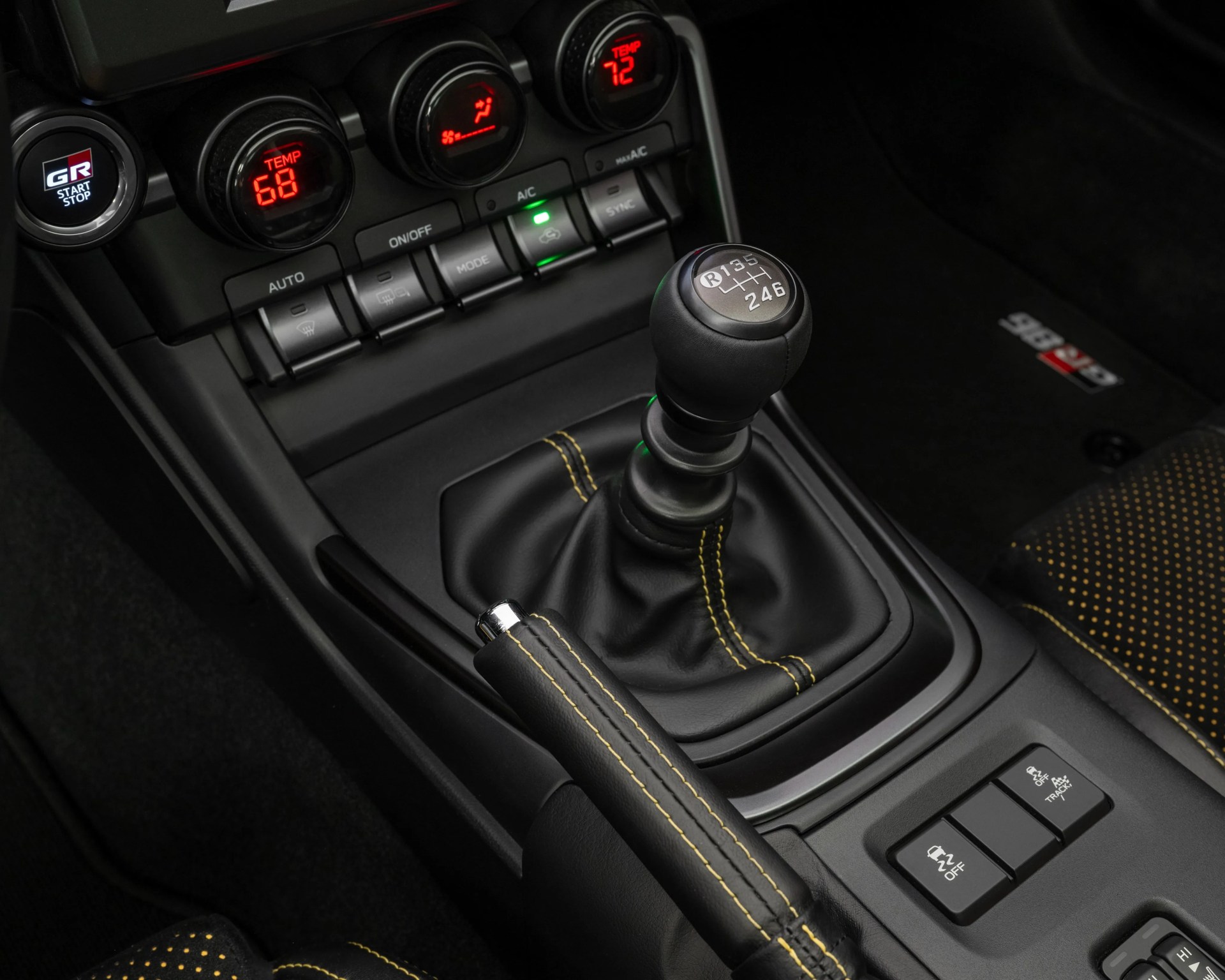 Black leather manual gear shift knob with yellow stitching and control buttons on a car center console.
