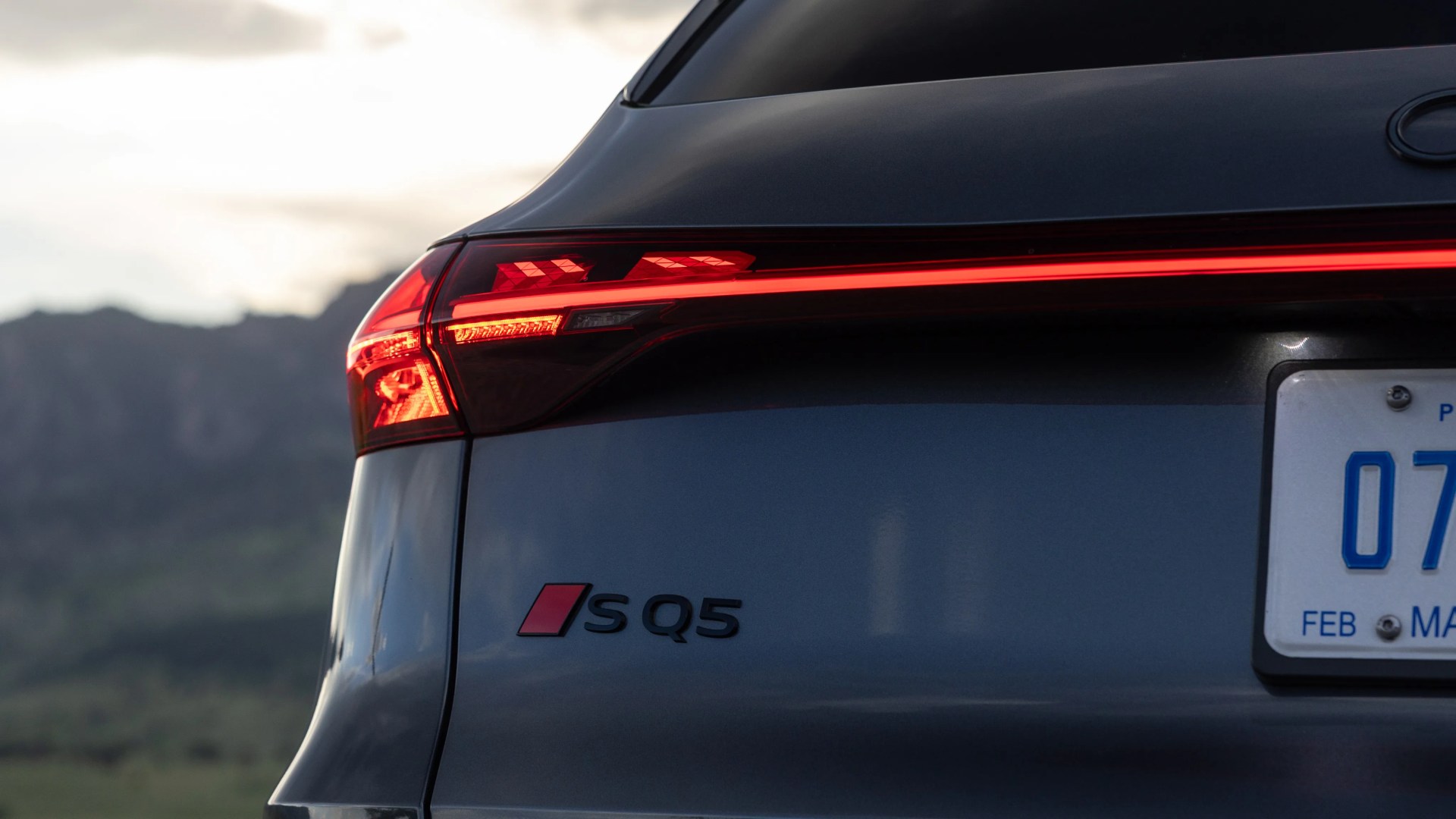 Rear view of a dark gray Audi SQ5 with illuminated taillight and partial license plate visible.