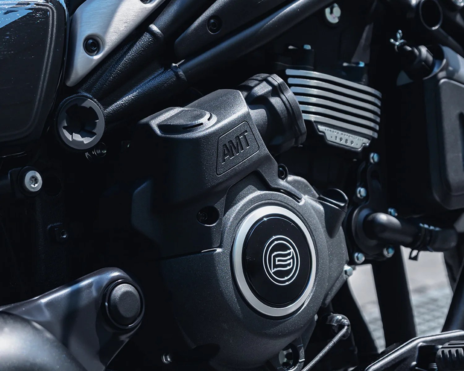 Close-up of a black motorcycle engine with "AMT" embossed on the casing and a circular emblem in the center.
